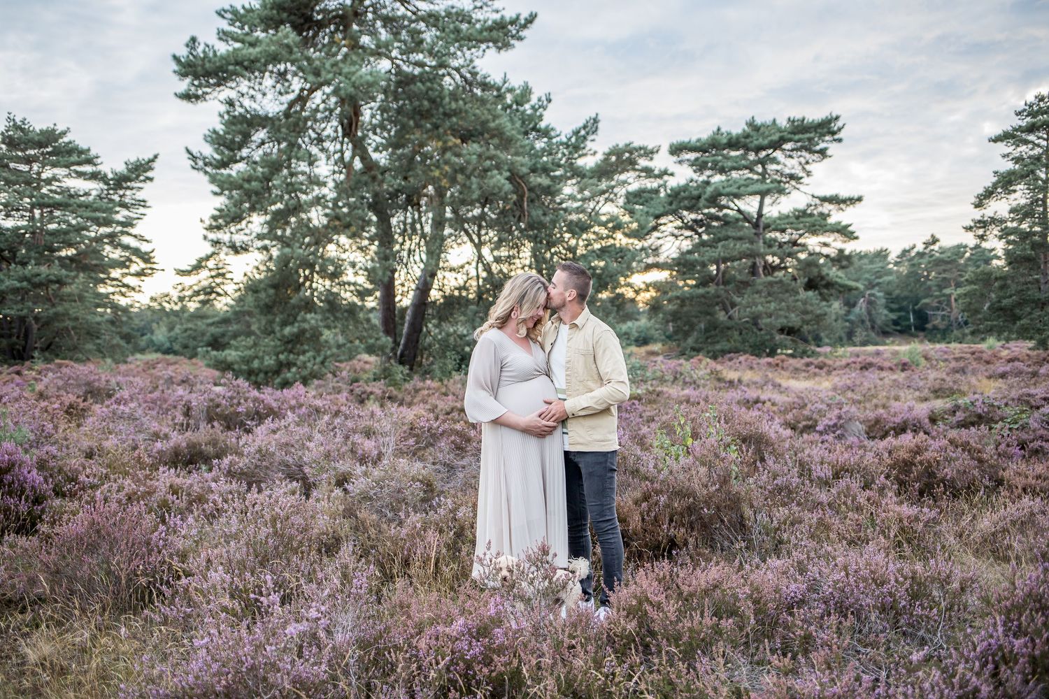 Pregnant couple sharing a tender moment in a stunning purple heather landscape at golden hour.