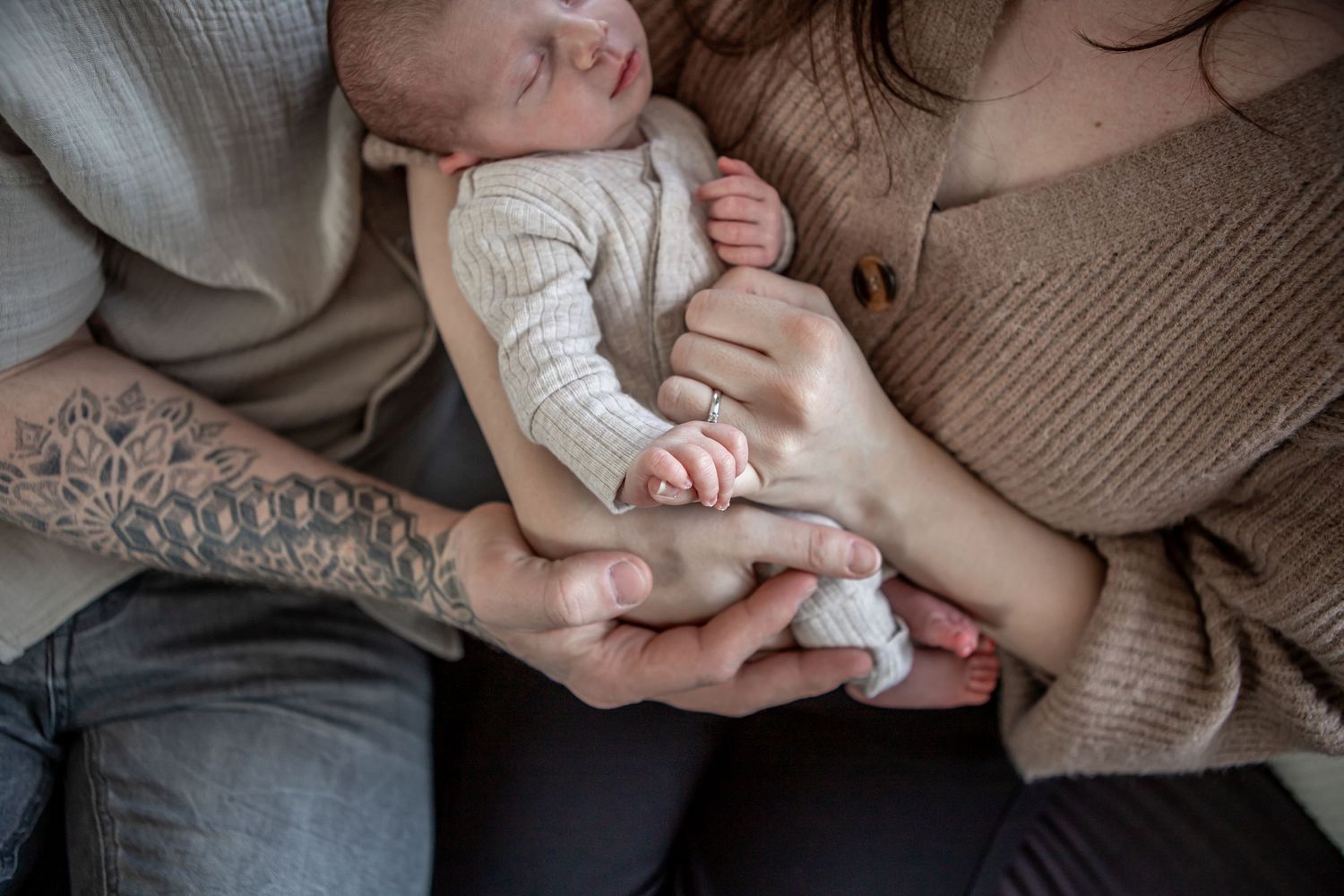 Parents cradling their newborn baby, with tattooed father's arm visible, tender family moment.