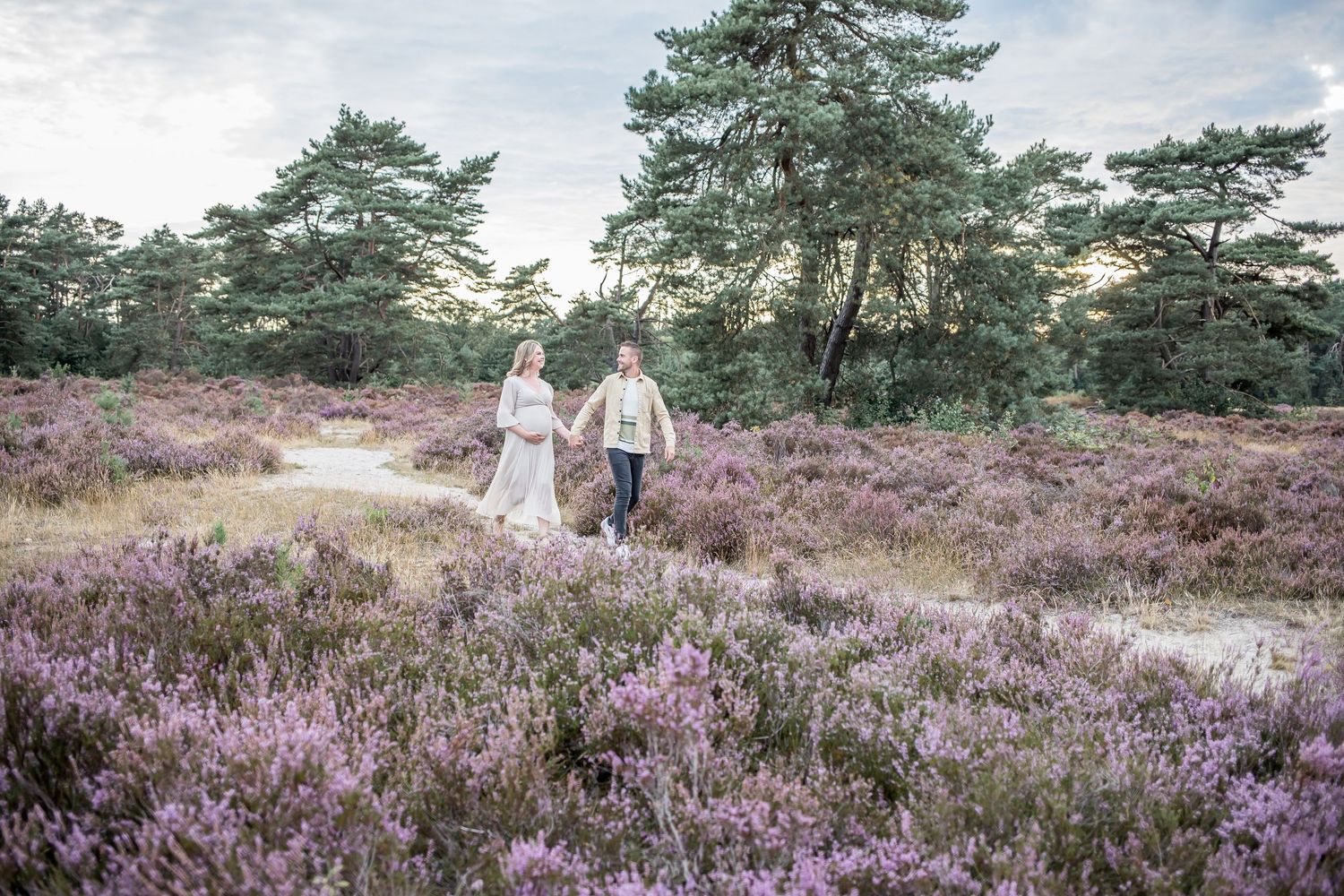Couple walking hand in hand through blooming purple heather fields at sunset.
