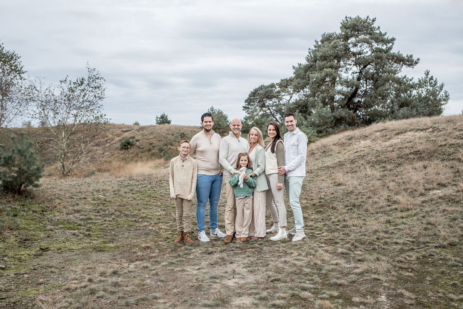 Extended multigenerational family of seven posing together on grassy hillside outdoors.