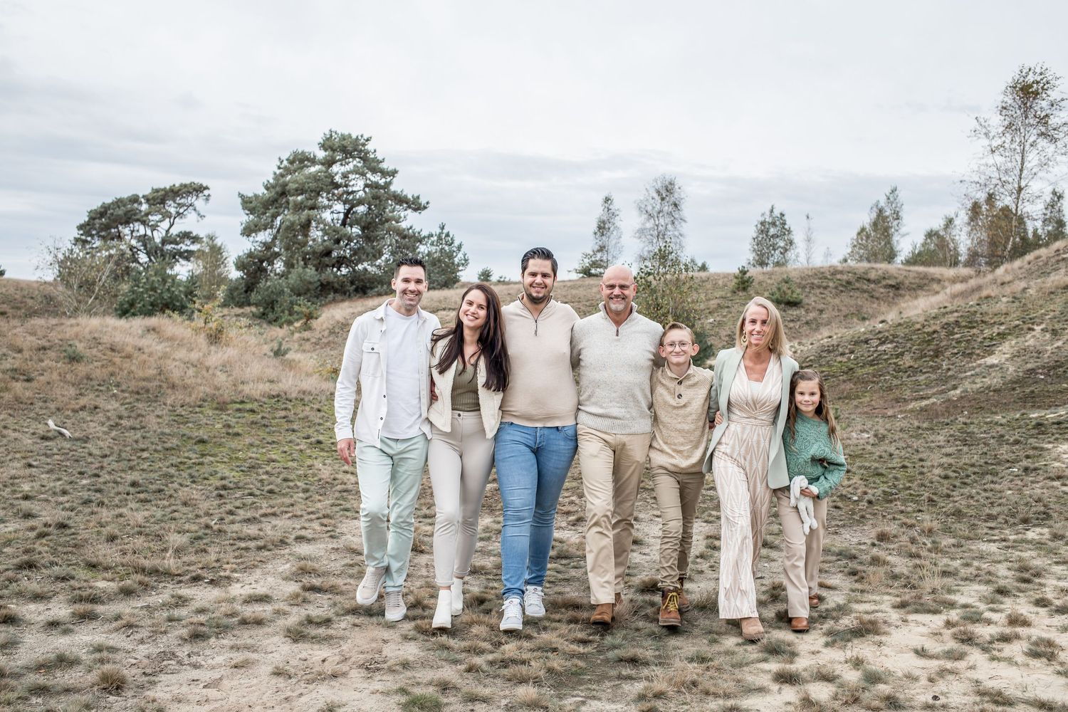 A multigenerational family of seven walks together smiling across a sandy open landscape.