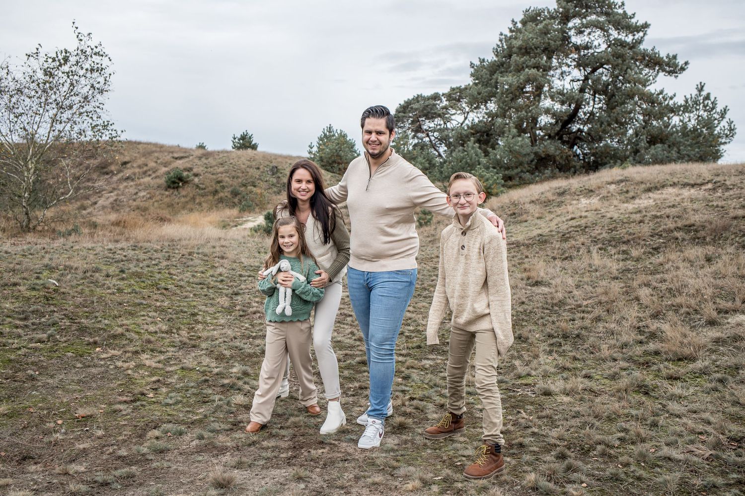 A family of four poses and smiles together on a sandy path surrounded by grassy dunes.