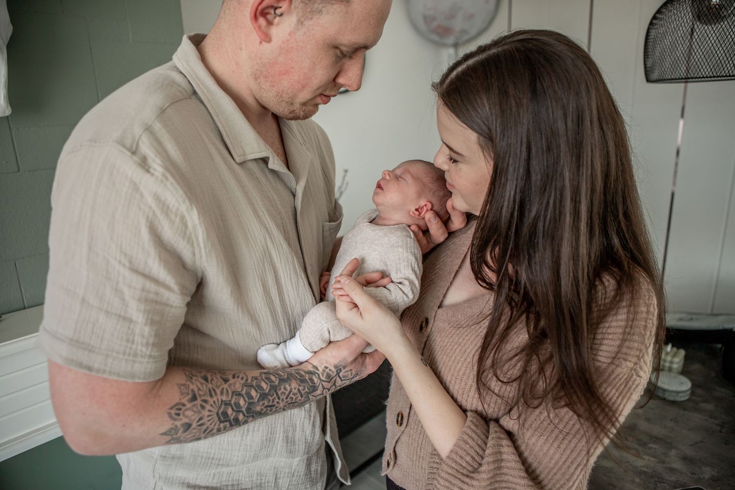 New parents lovingly gazing at their newborn baby together in a softly lit bedroom.