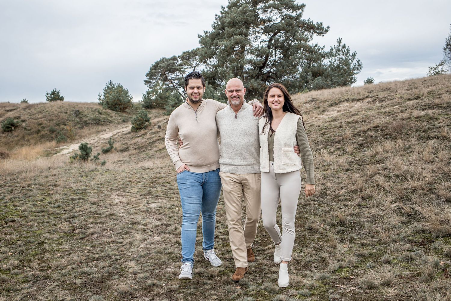 Two young men and a woman pose together smiling on a hillside with pine trees behind them.