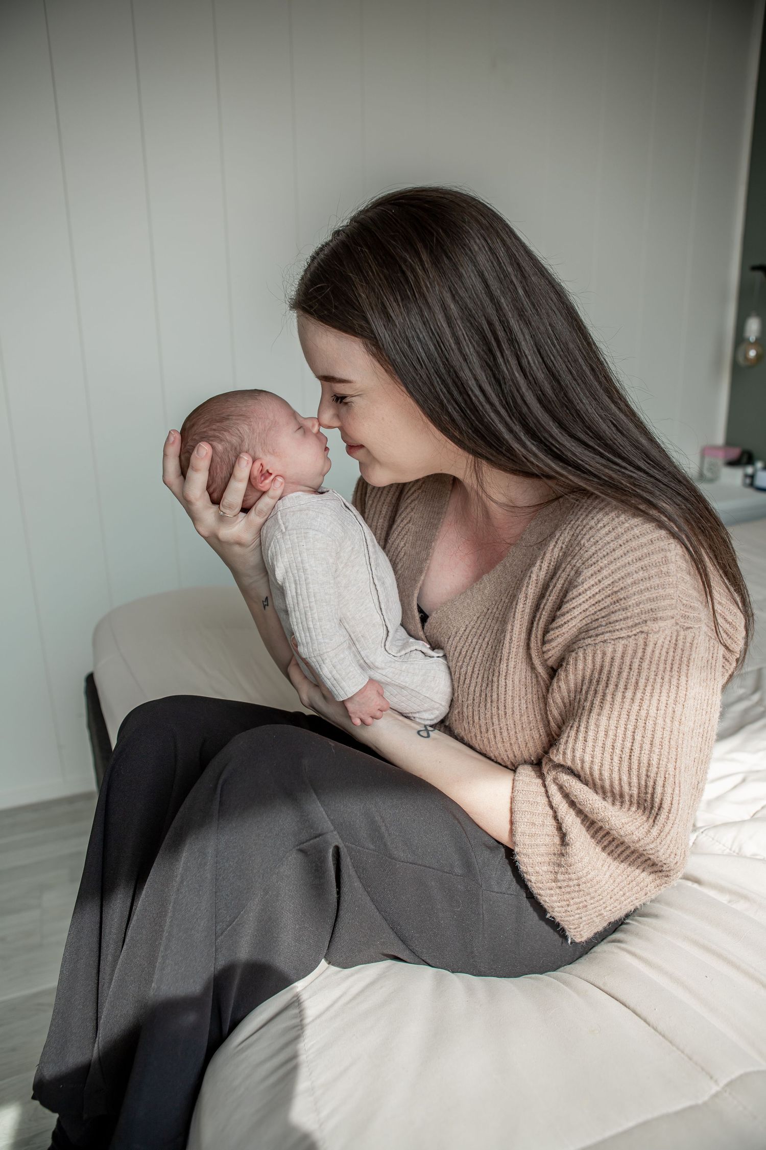 Loving dark-haired mother tenderly touching noses with her newborn baby while seated indoors.