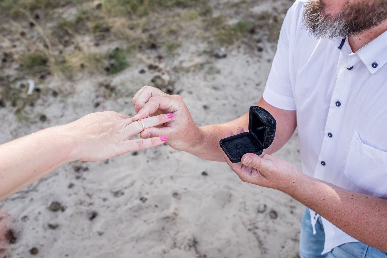Close-up of man placing engagement ring on womans hand from open ring box.