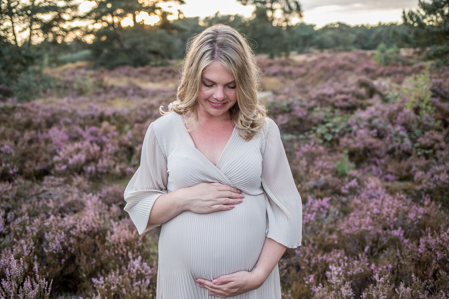 Pregnant woman in elegant grey wrap dress lovingly cradling her baby bump in purple heather.