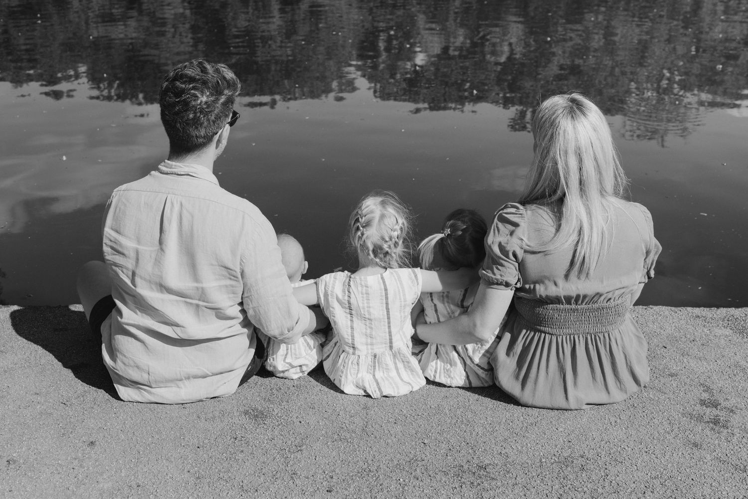 A family sits together by a lake enjoying a peaceful moment in black and white.