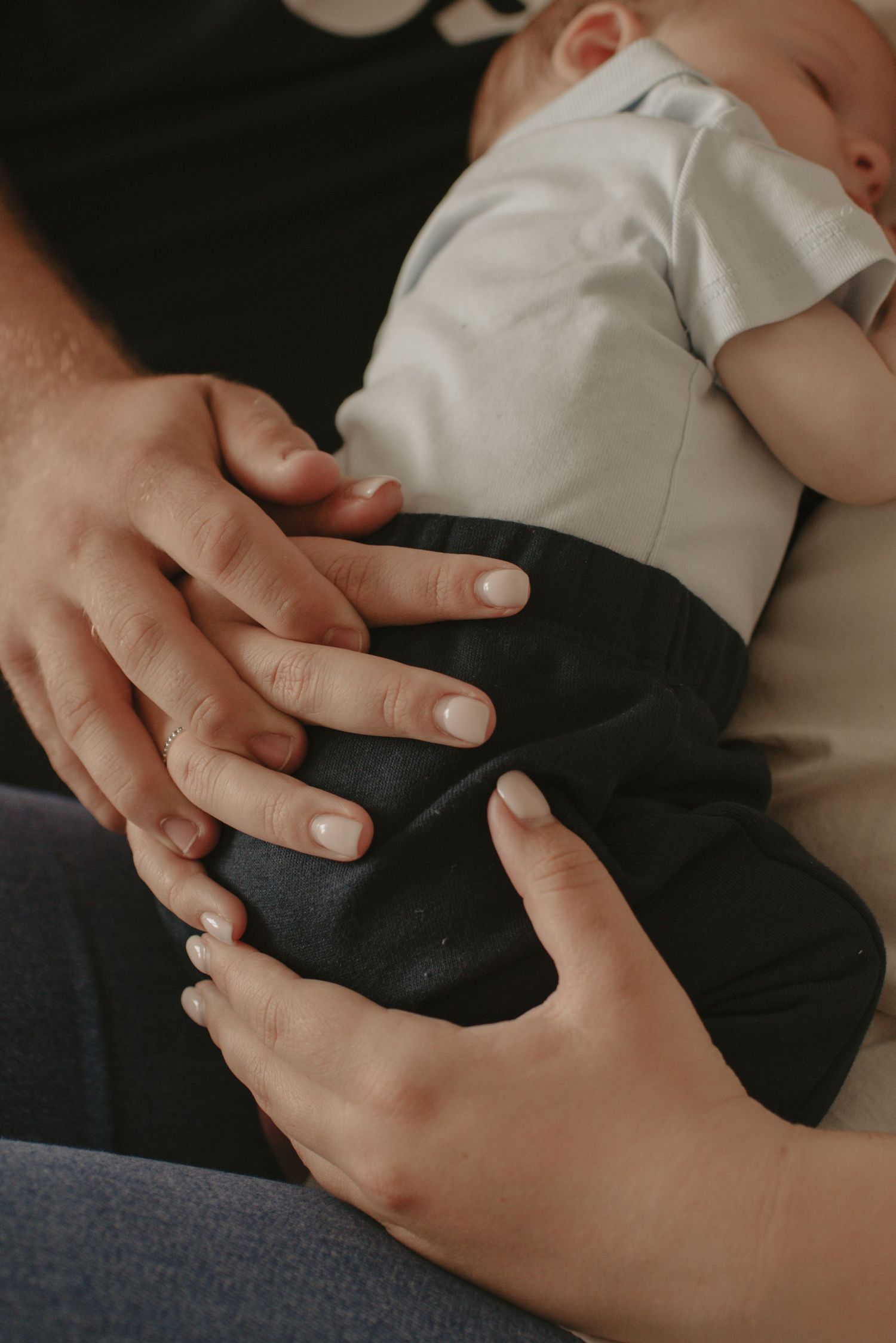 Close-up of hands gently resting on a sleeping baby wearing white and black clothing.