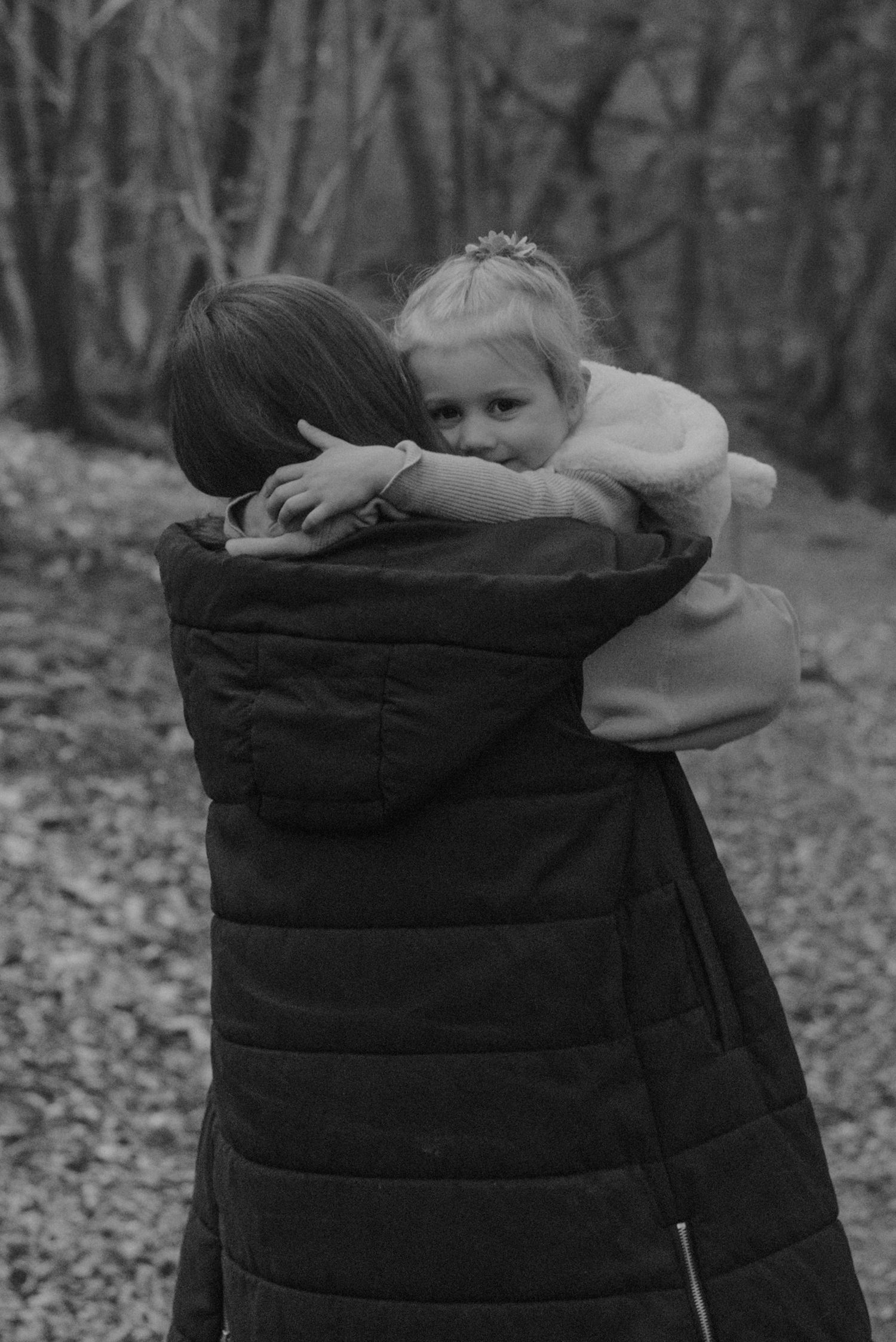 Black and white photo of child hugging adult in puffy winter coat outdoors.