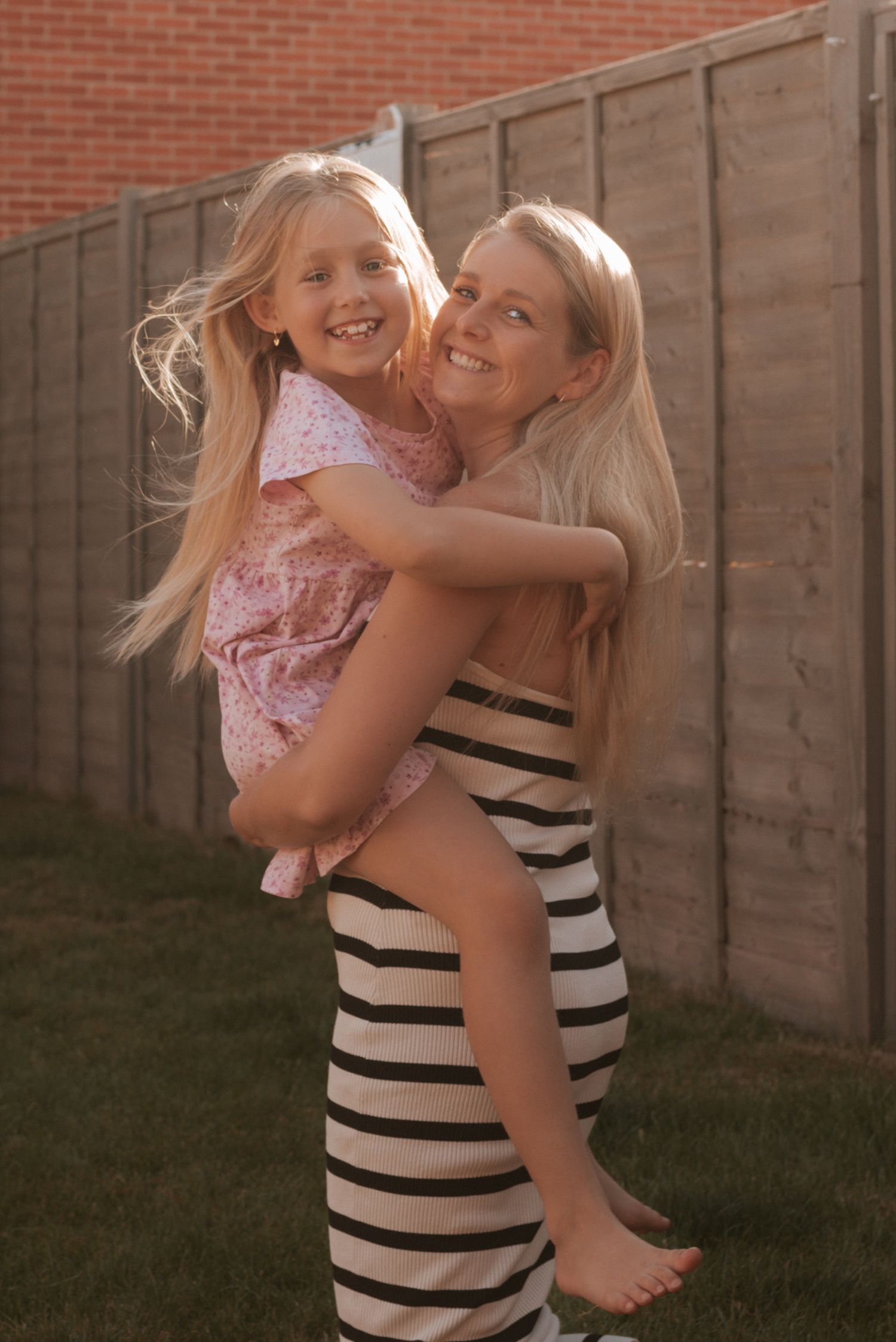 A heartwarming outdoor portrait shows a loving embrace between two people in a backyard with a wooden fence background.