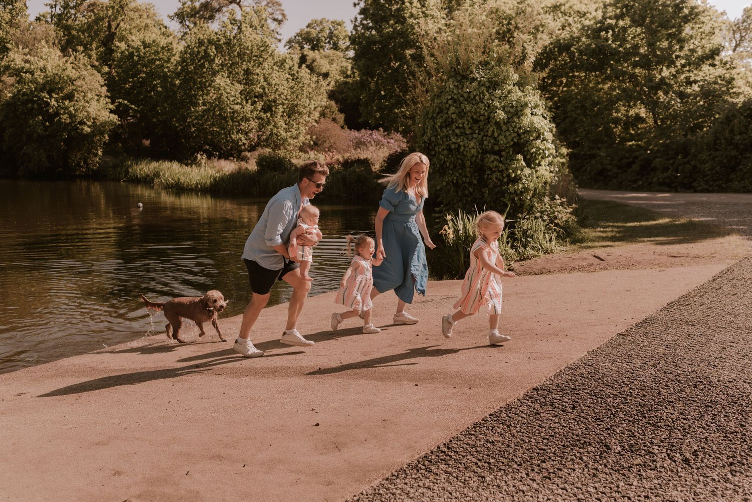 Family runs along a path by the river with their dog on a warm afternoon.