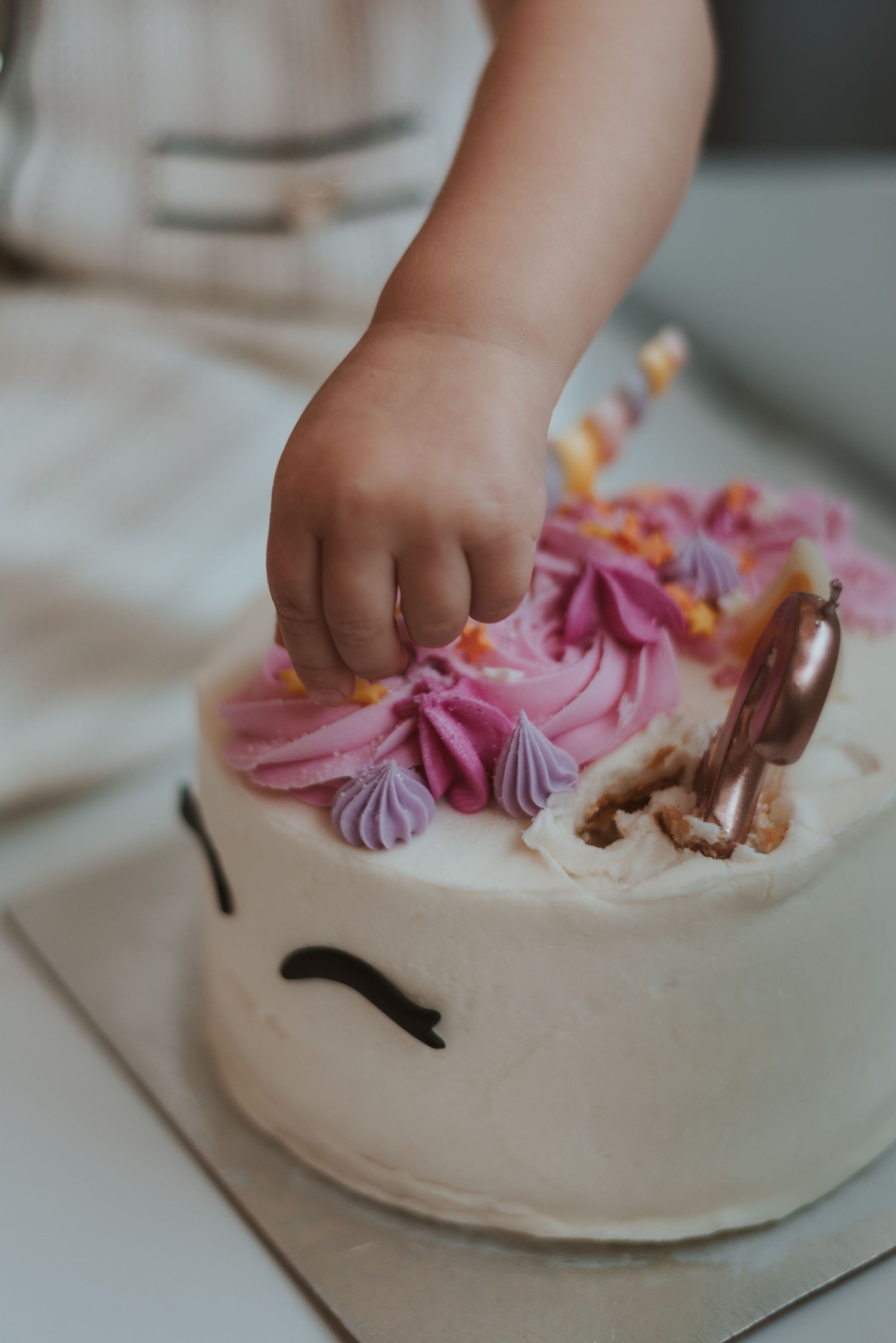 Small hands reach for pink frosting decorations on a white cake.