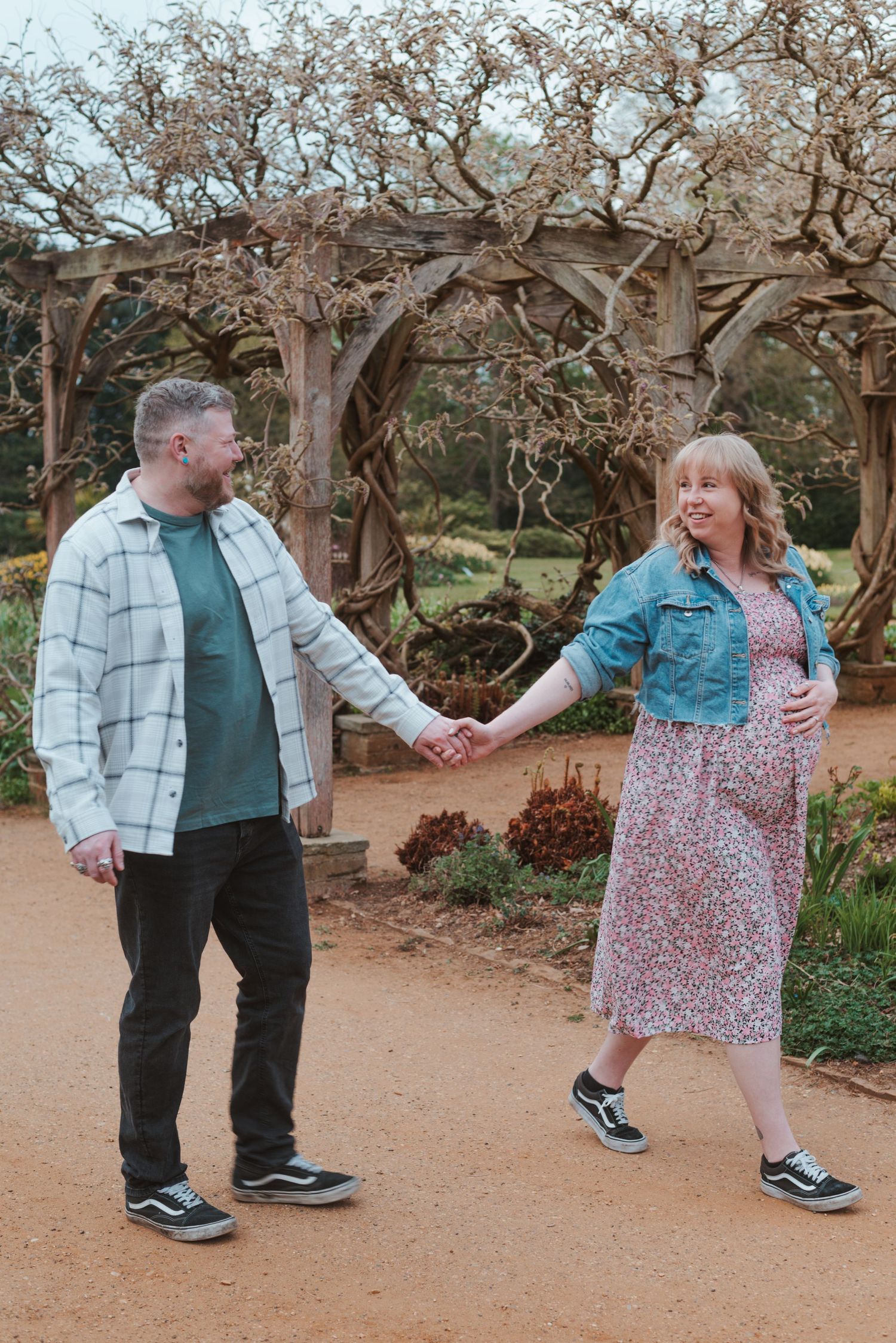A playful outdoor maternity photoshoot under twisted trees on a dirt path.