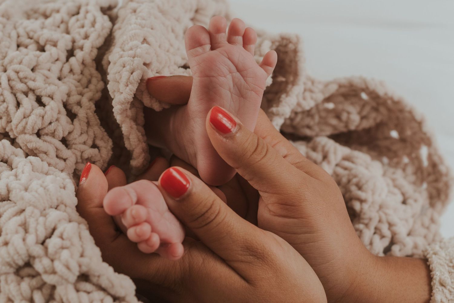 Close-up of tiny baby feet being gently held by hands with red nail polish.