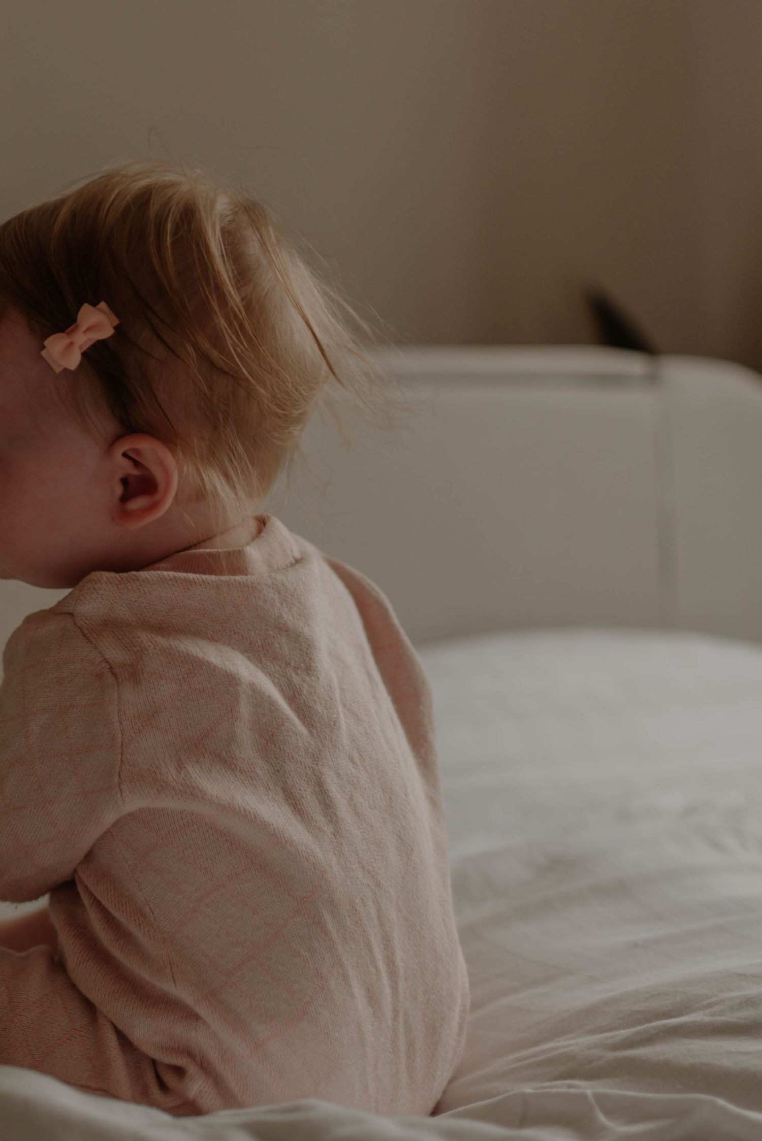 A series of soft, intimate close-up photos showing a baby in white clothing lying on light bedding.