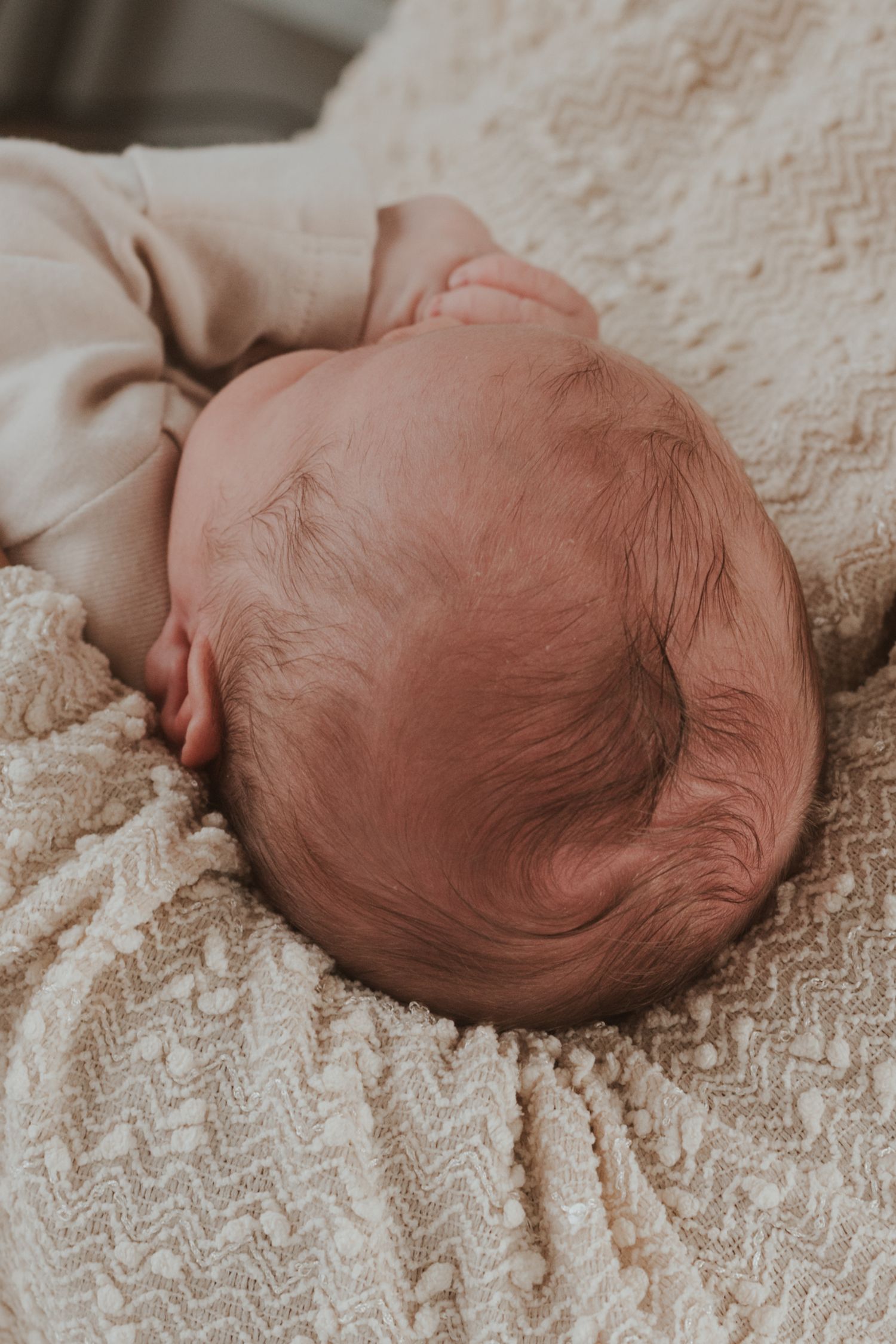 Baby resting on textured cream blanket with soft natural lighting.