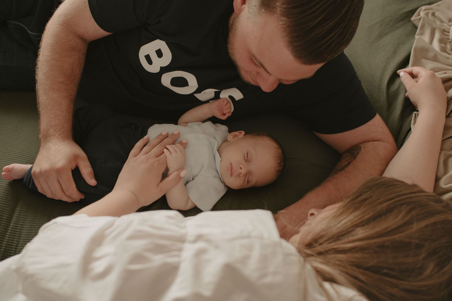 Intimate family moment captured on dark couch with baby in white clothing.