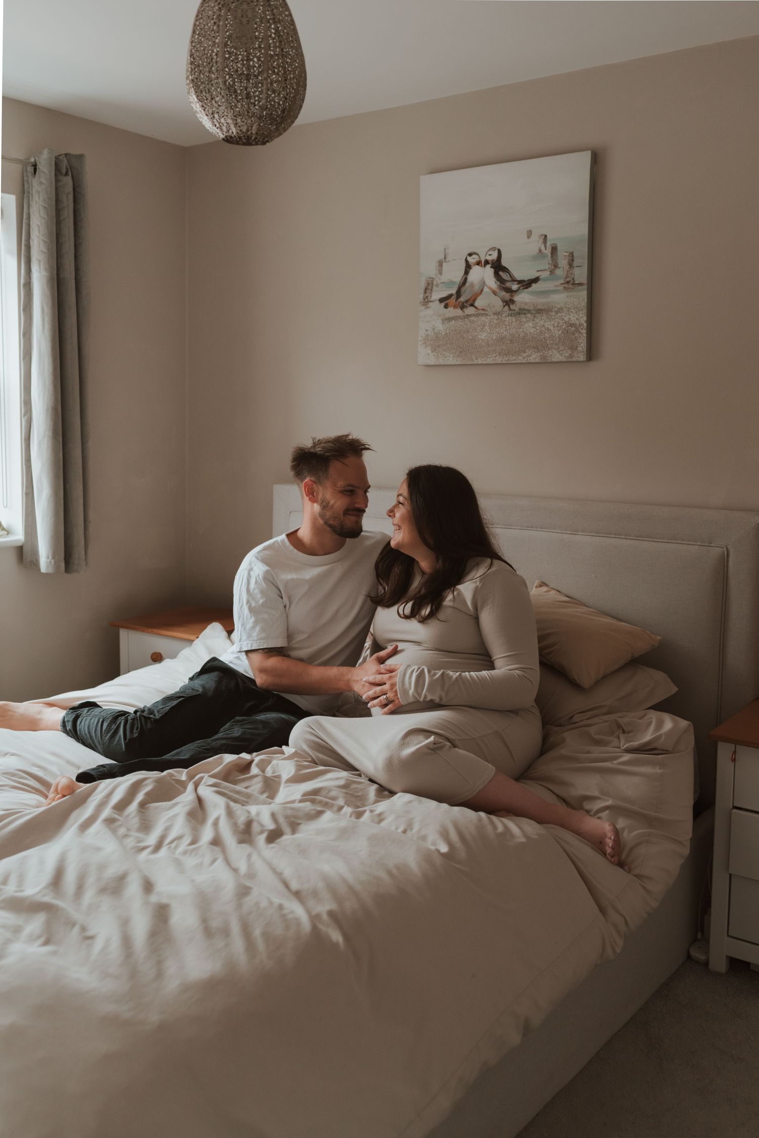 An intimate maternity photo session in a cozy bedroom with neutral tones and soft lighting.