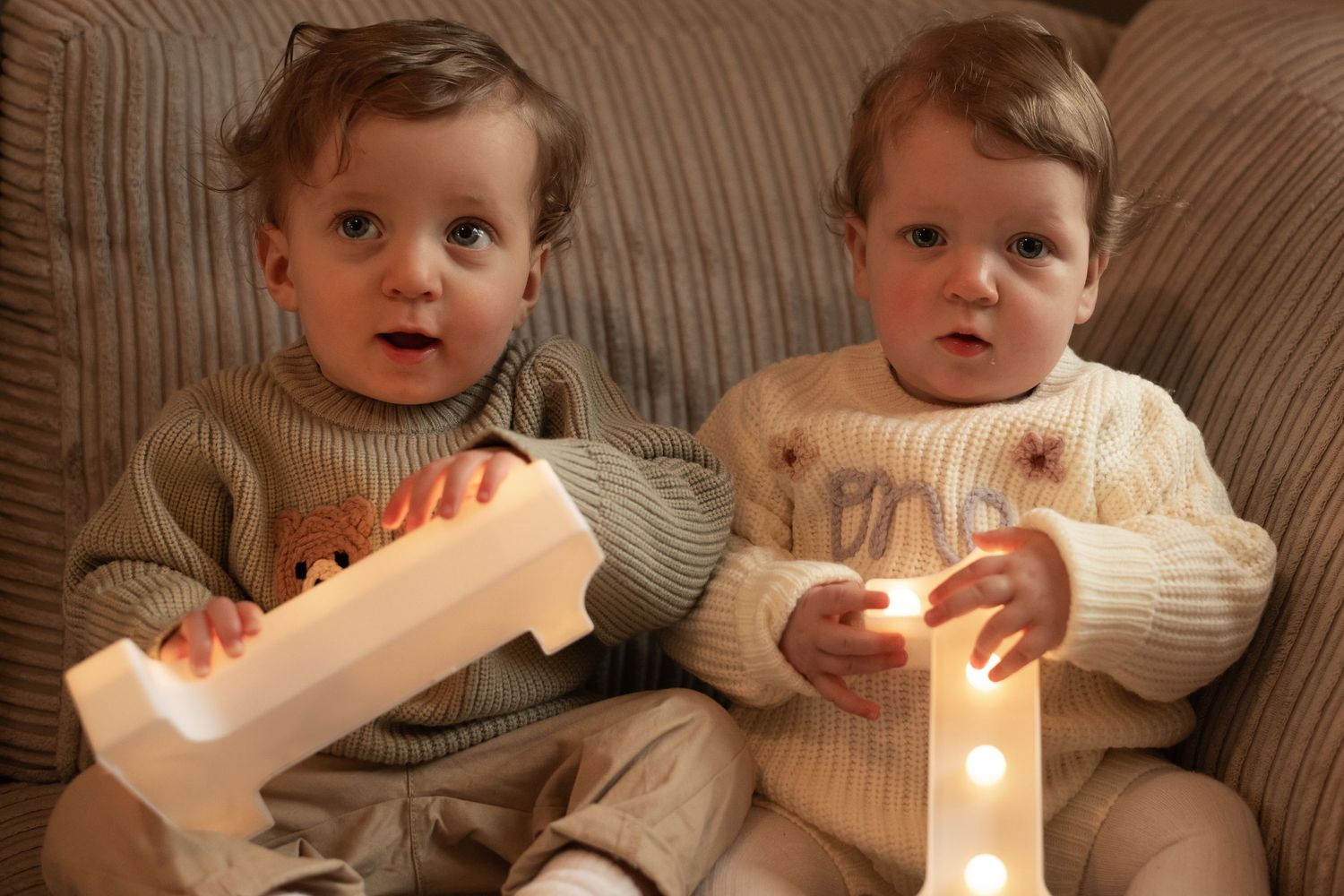 Baby in cream sweater playing with glowing number one candle.