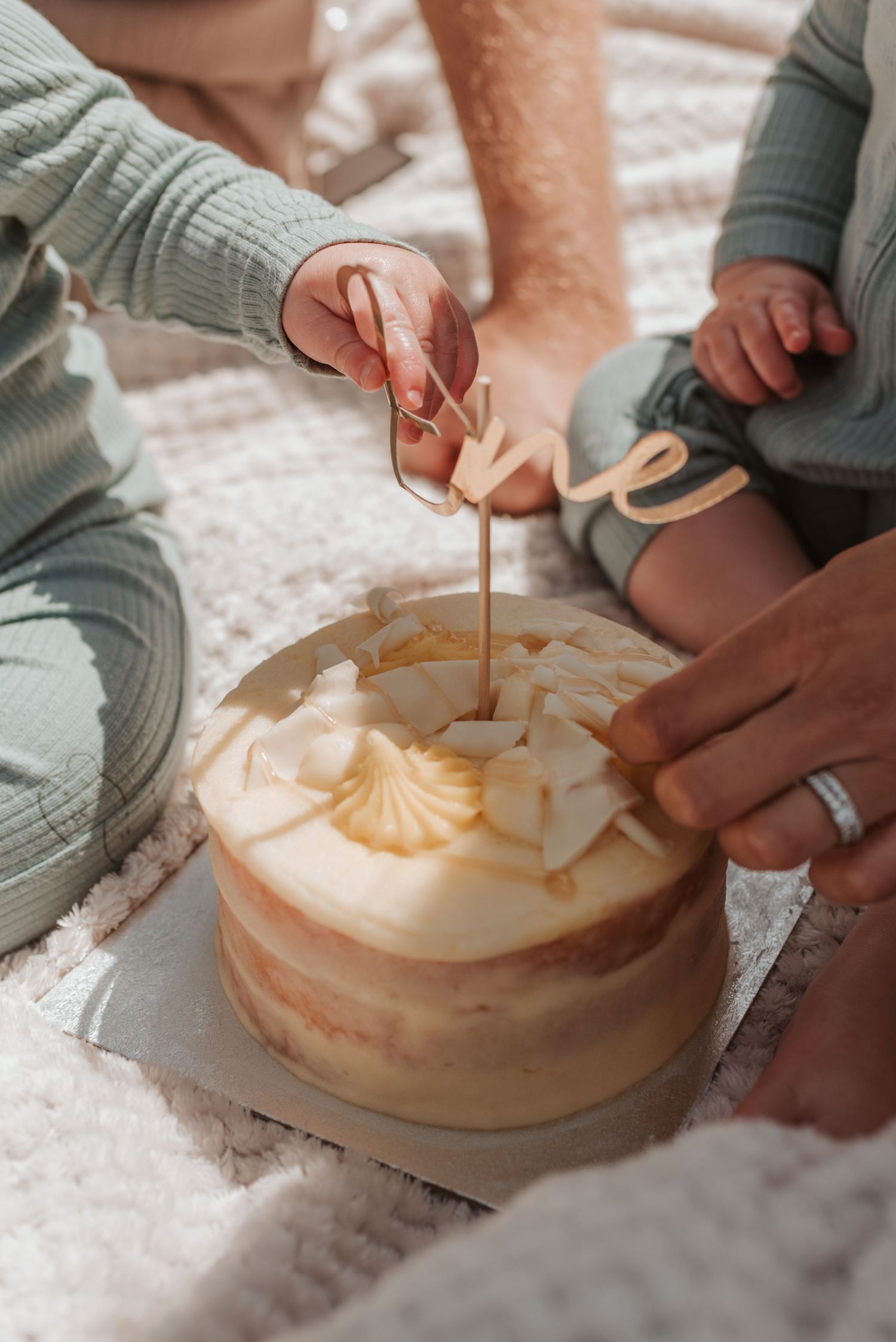 Two people sit together on a blanket cutting into an elegant white meringue-topped cake with almond slices.