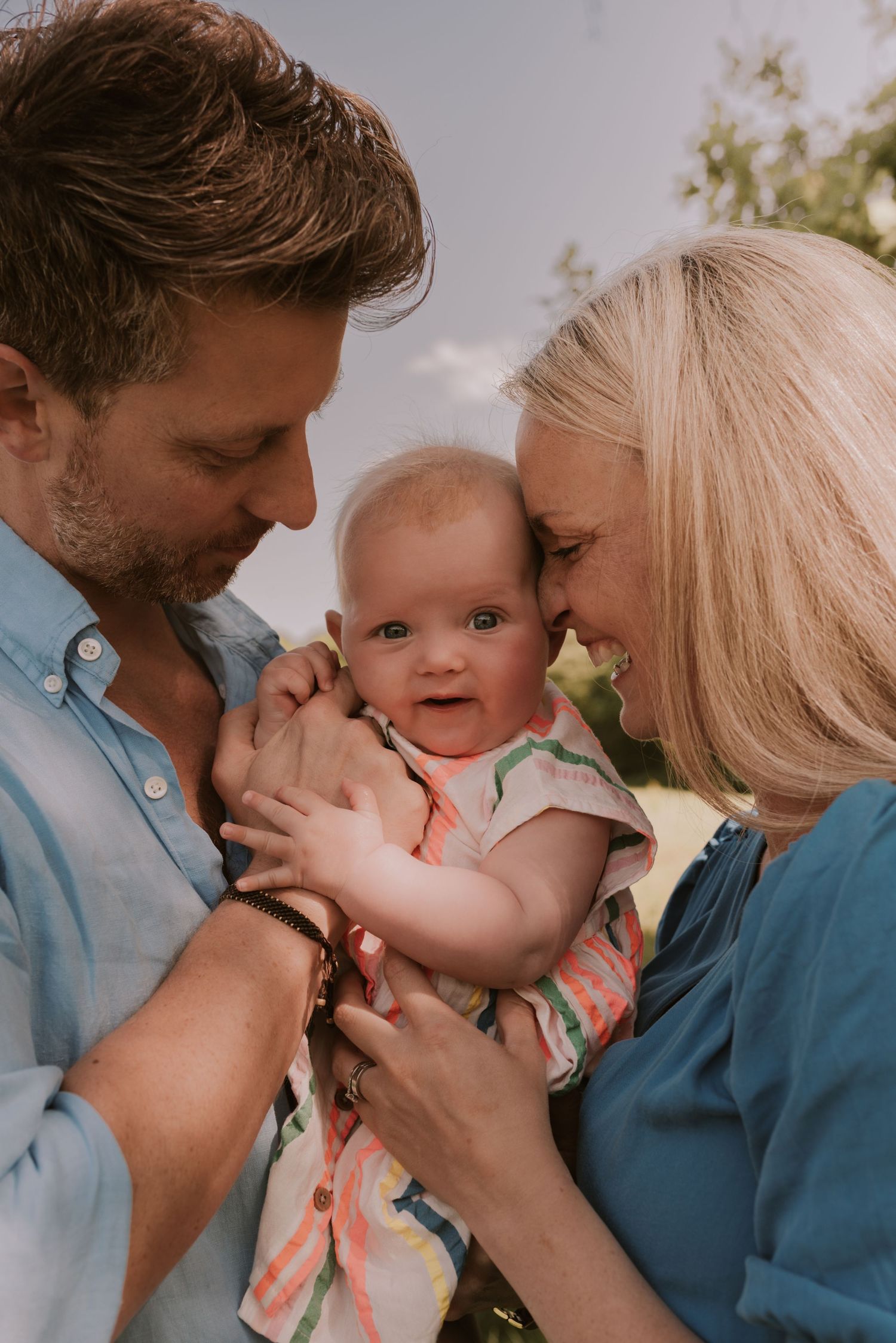 A tender family moment outdoors with a smiling baby in the center.