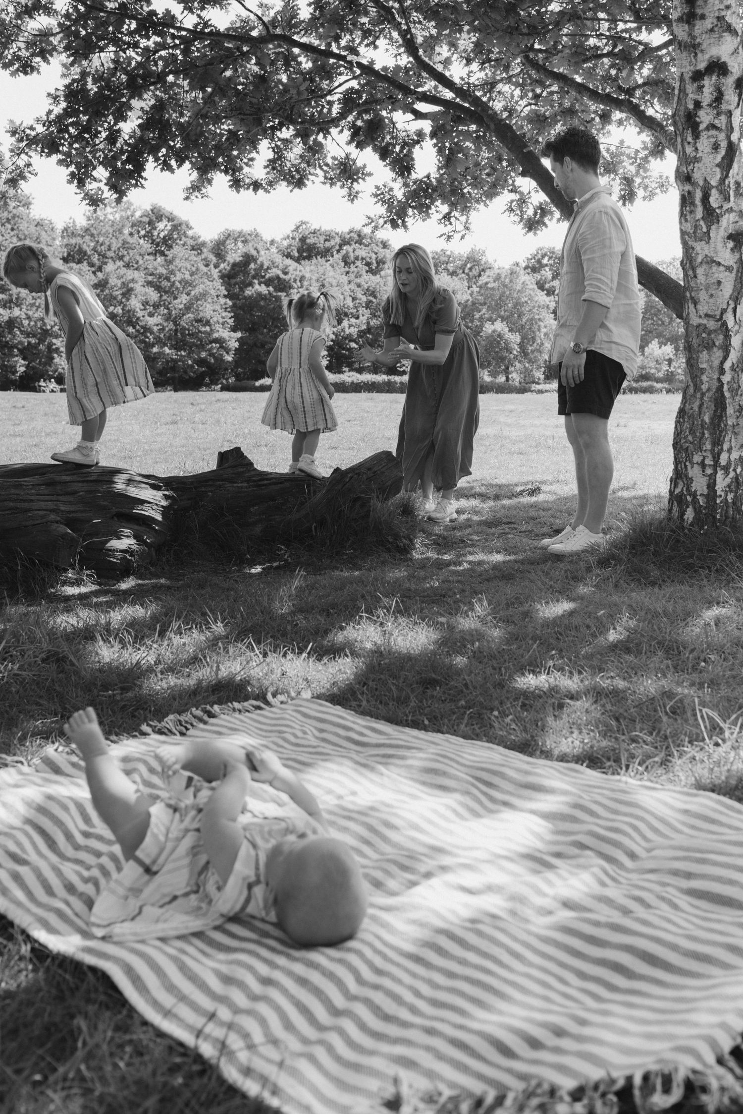 Black and white photo of a family gathering under trees with a striped blanket picnic setup.