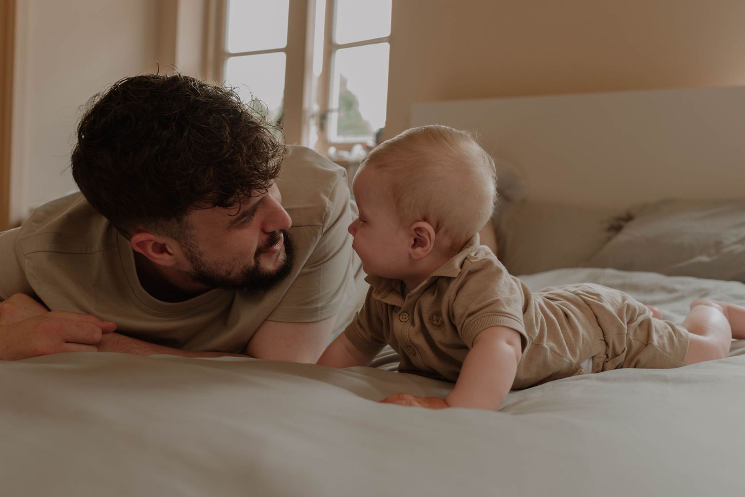 A parent and baby lying together on a white bed sharing a tender bonding moment.