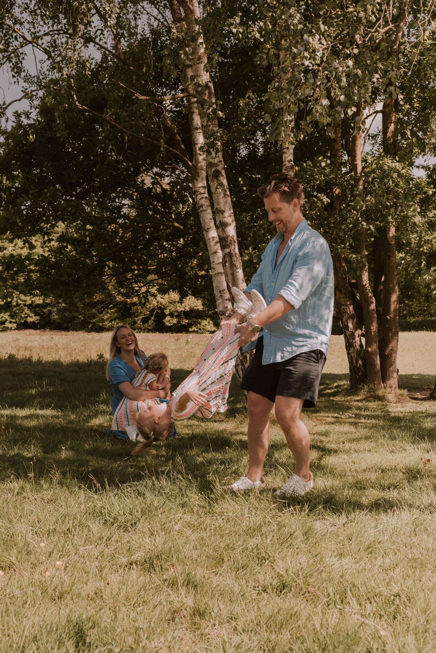 Family playtime in a garden with someone swinging a child while others watch from nearby.