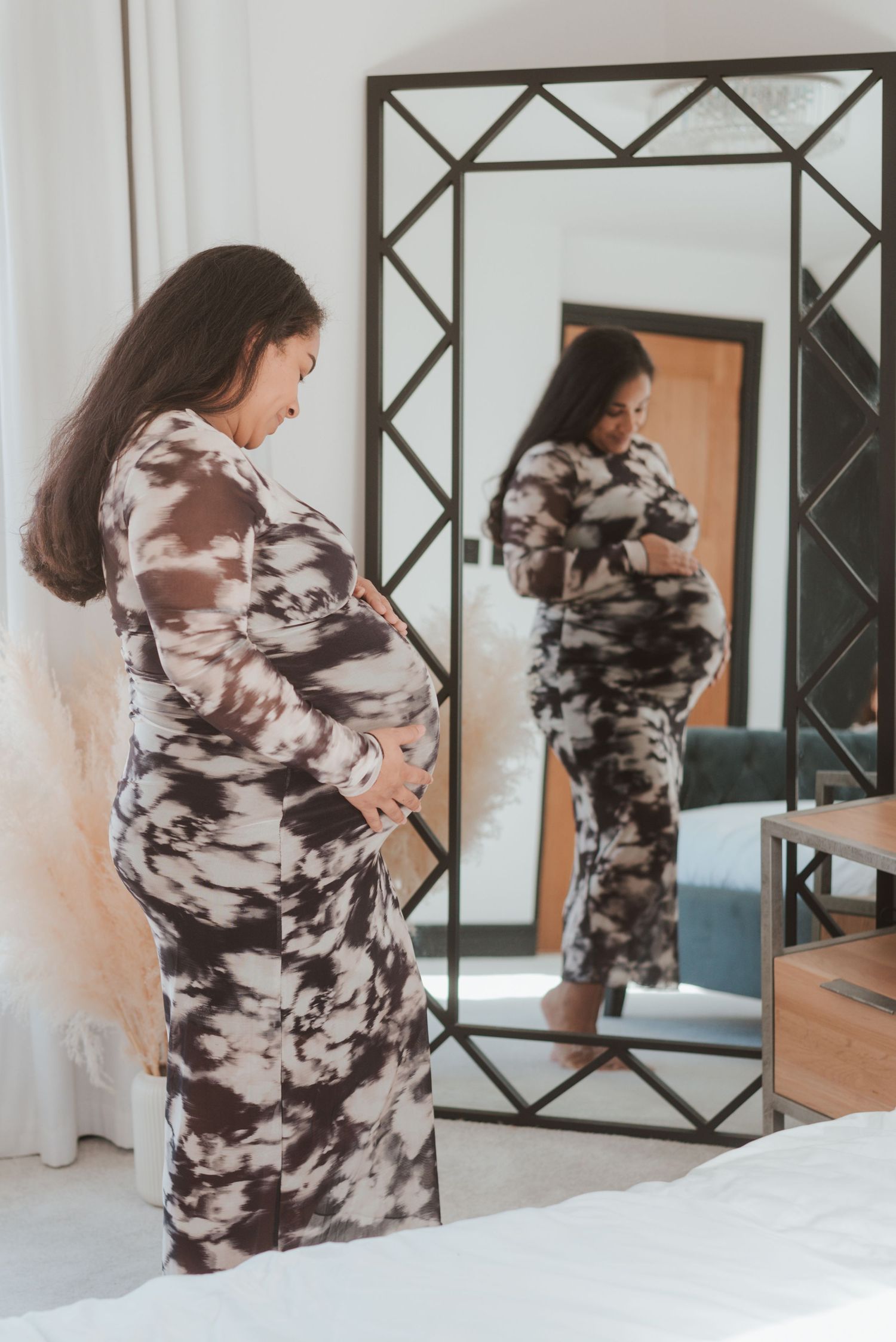 Figure in a flowing black and white dress poses near geometric mirrors and natural window light.
