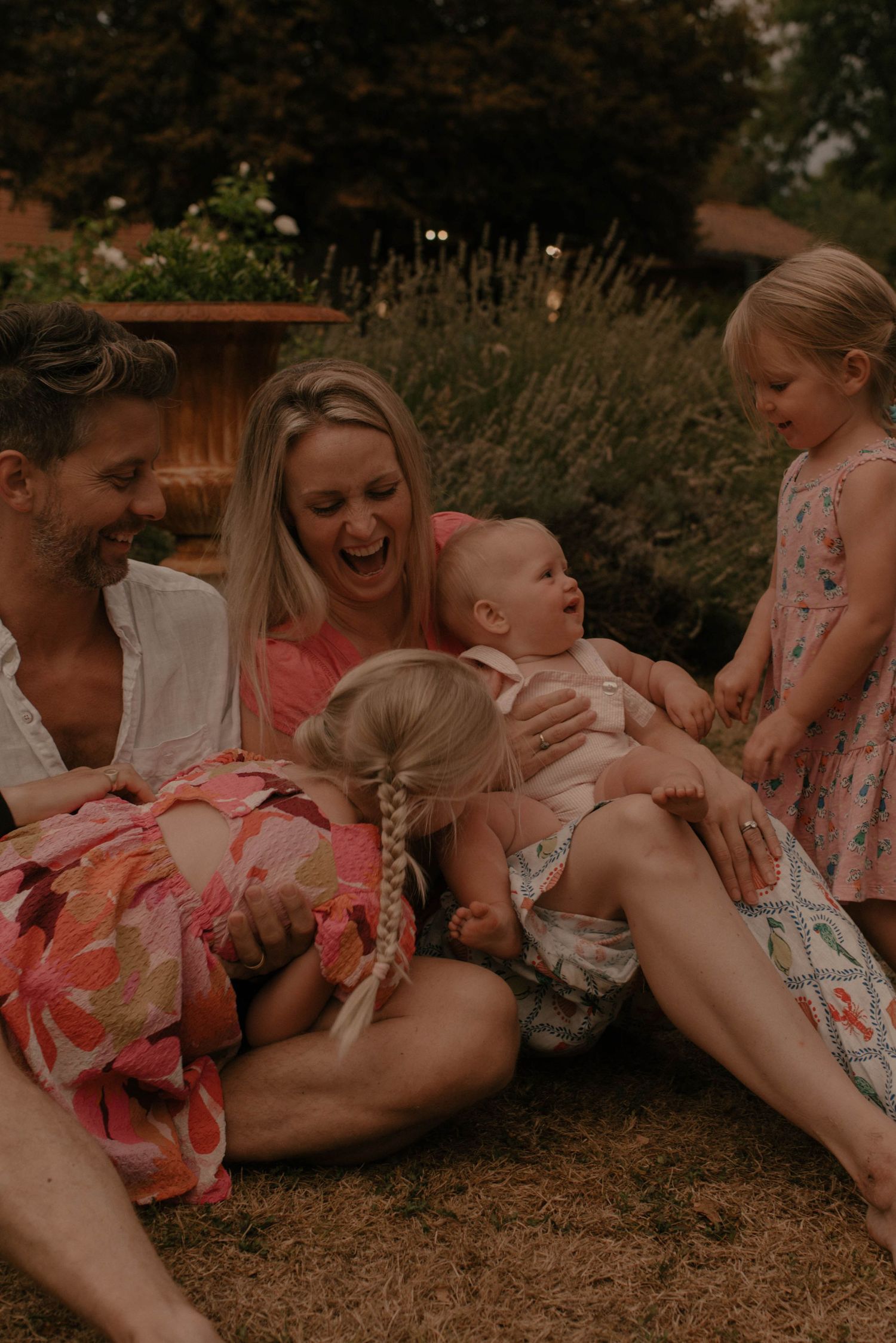 A group of people wearing pink and white outfits lay together on the ground in a candid outdoor photo series.