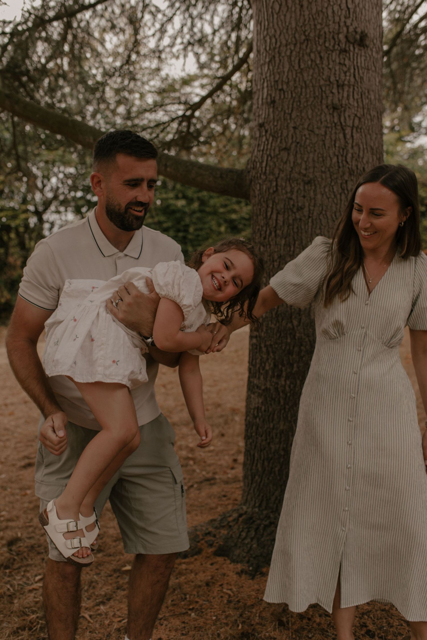 Candid outdoor photo series showing playful couple laughing and embracing under trees on forest floor.