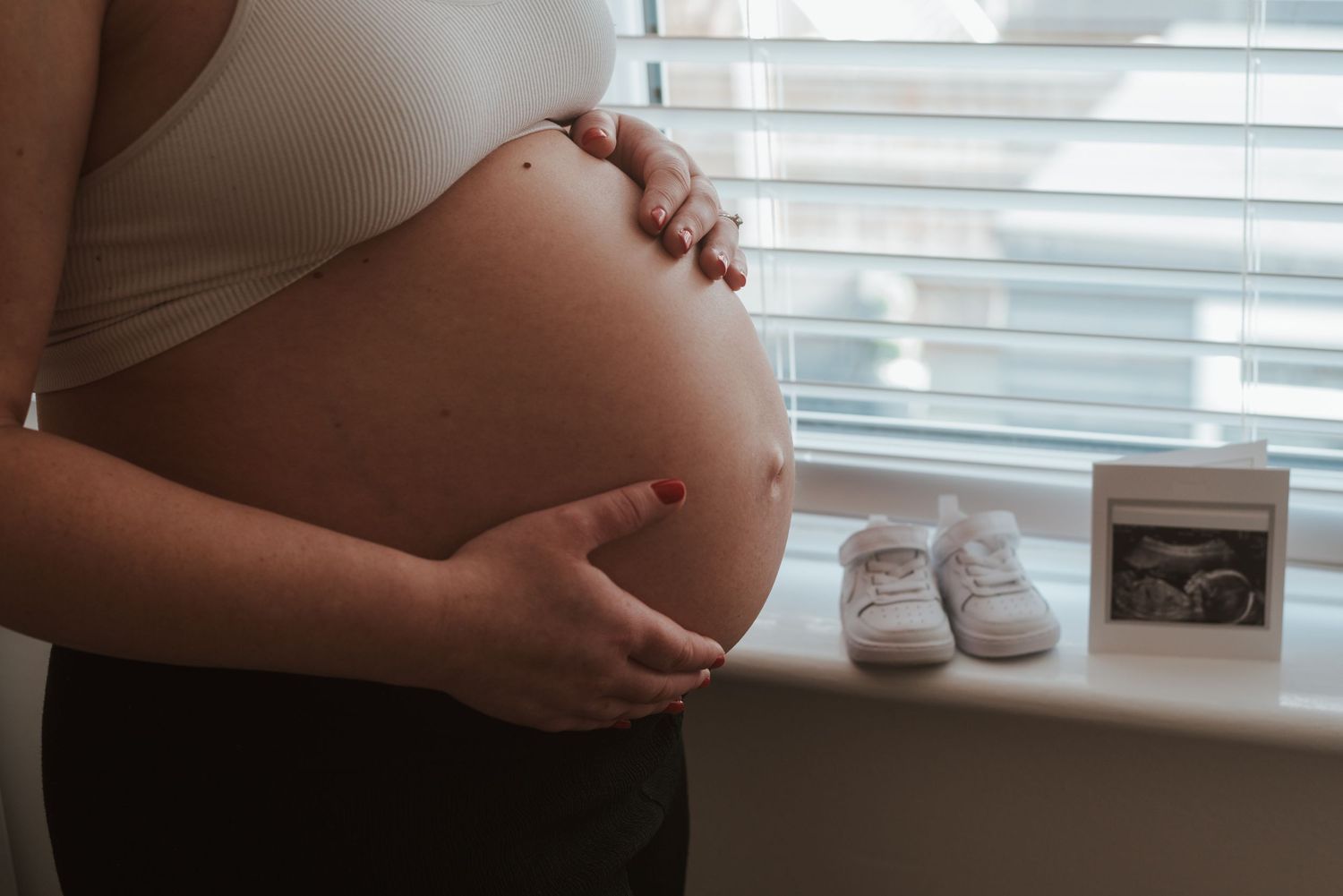 Close-up shot of a pregnant belly with tiny baby shoes resting on top.