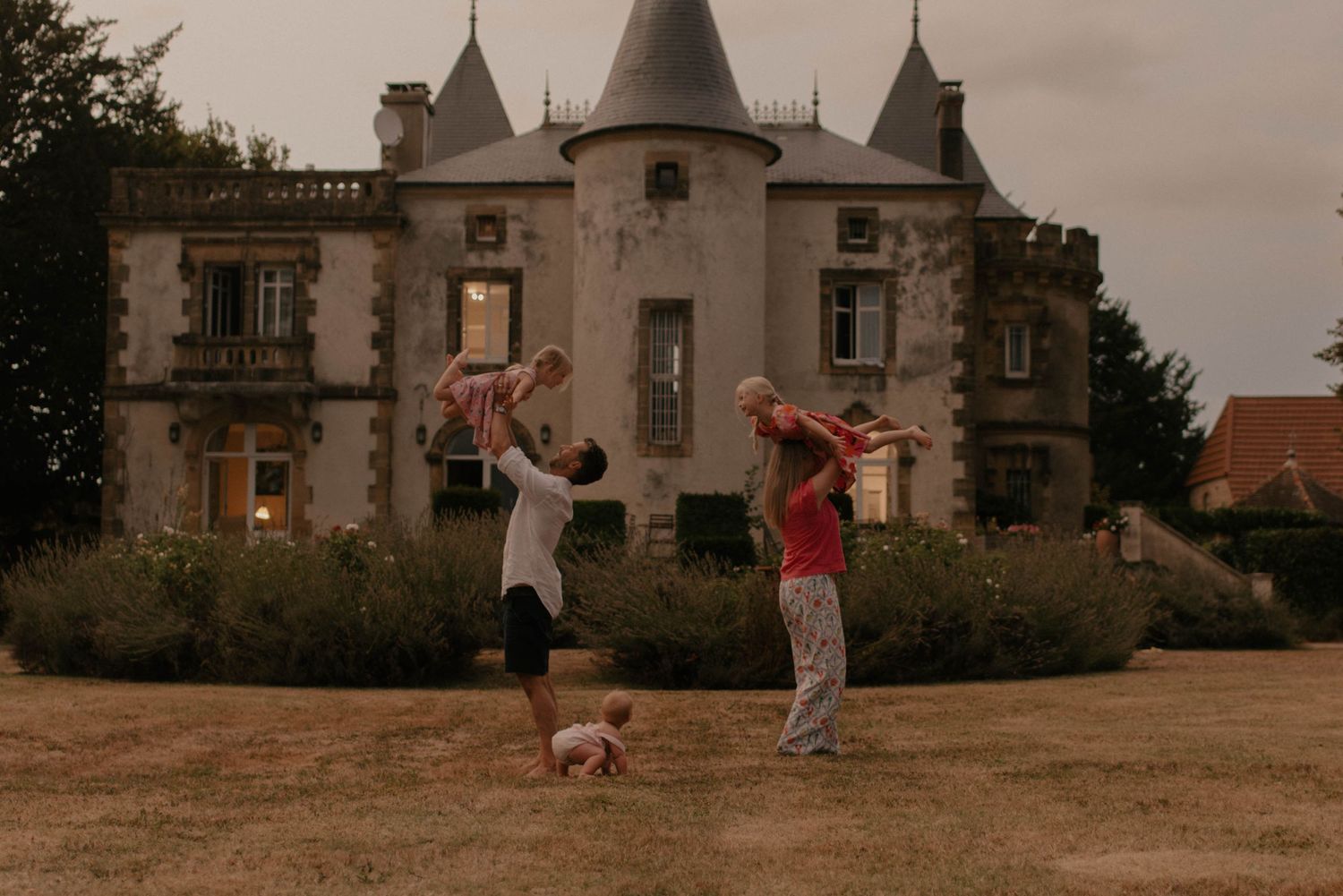Two people dancing playfully in front of a grand chateau with turrets at sunset.