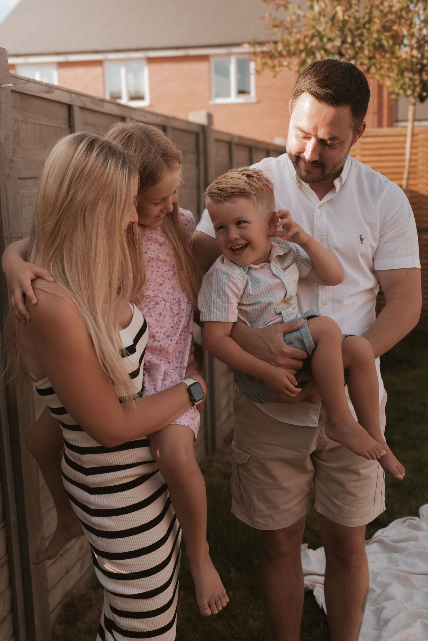 Two adults and a young child share a joyful moment together outdoors in a backyard during golden hour.