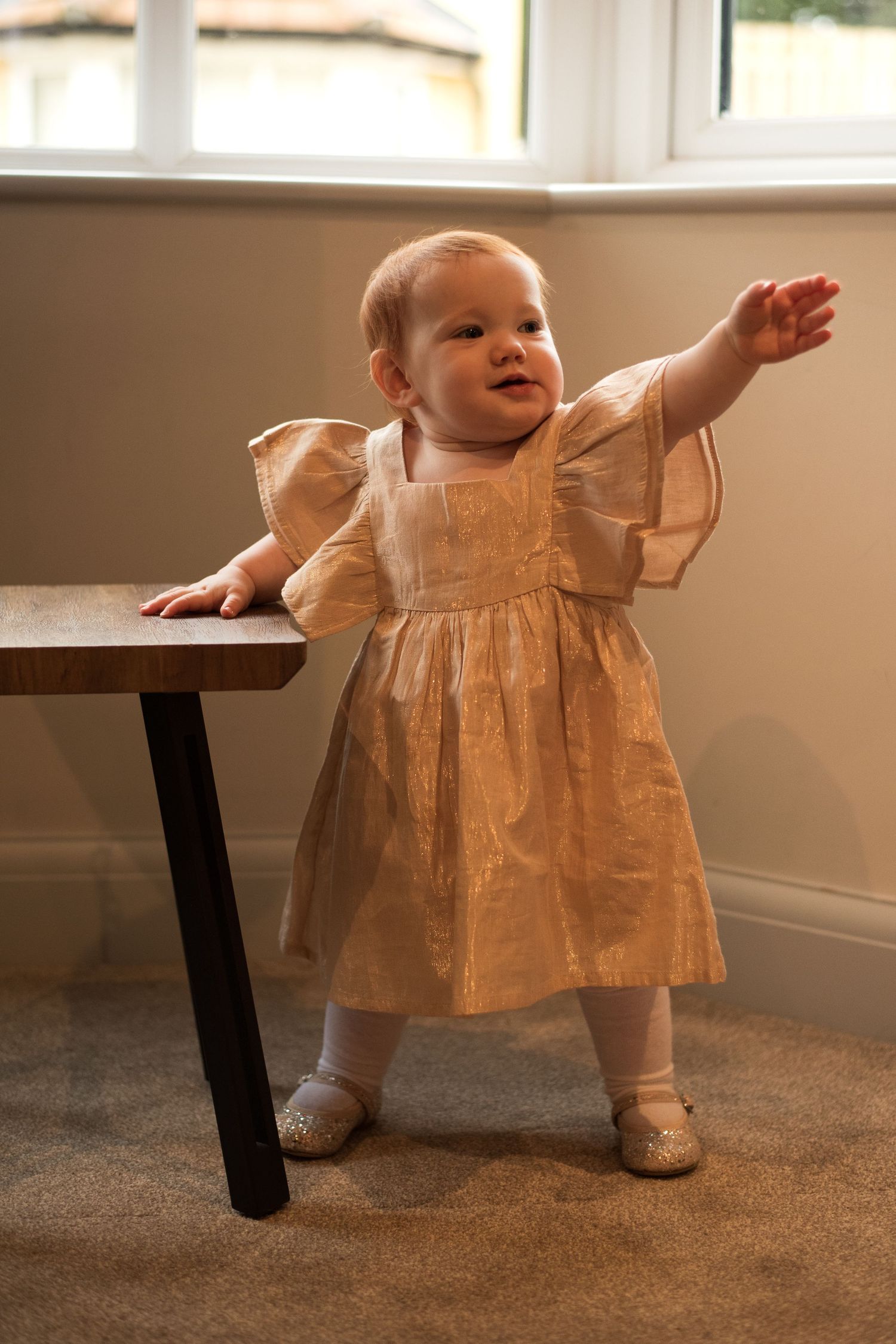 Small feet in a sparkly gold dress move across a carpeted floor.