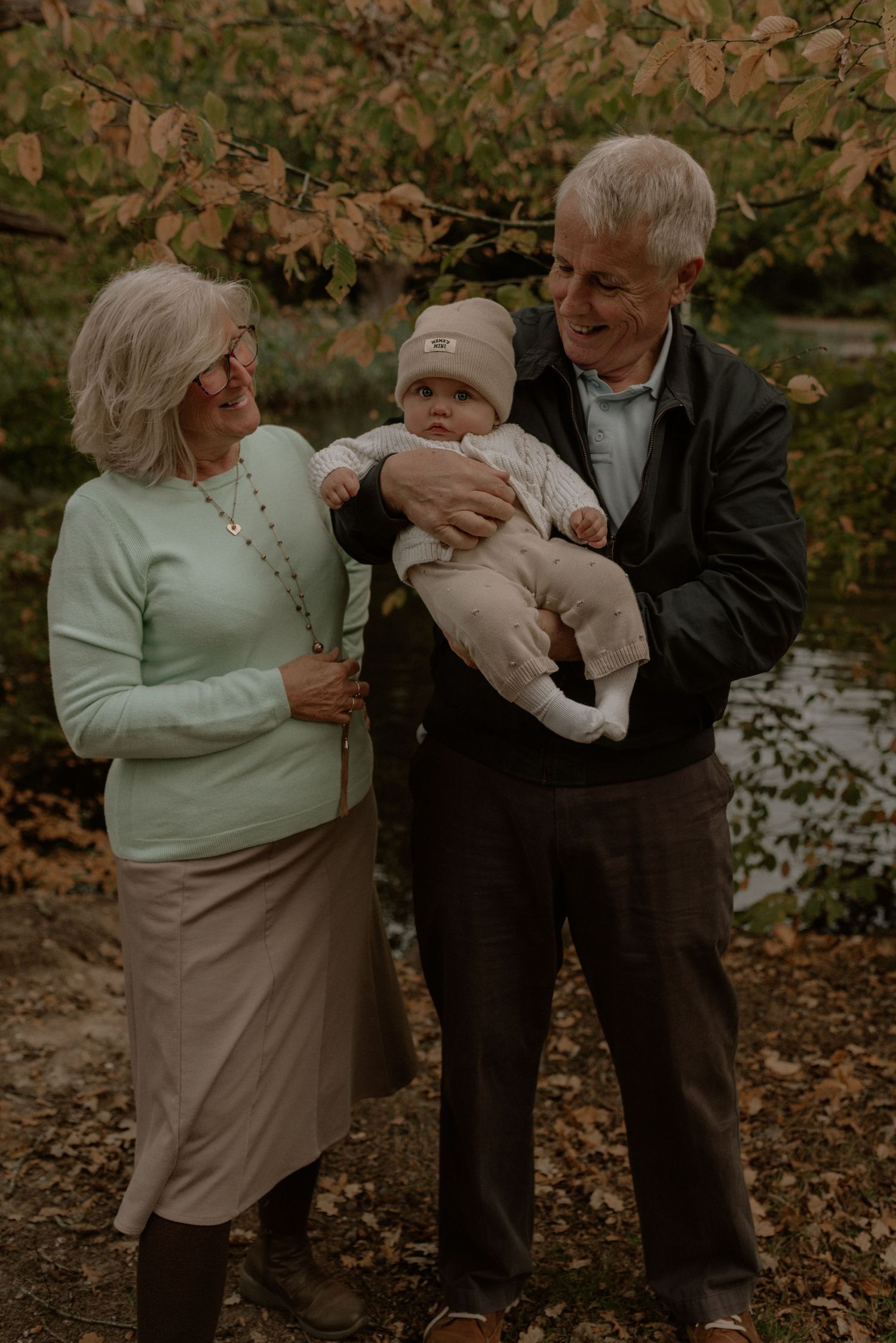 A couple in autumn scenery shares tender moments while holding a small baby outdoors.