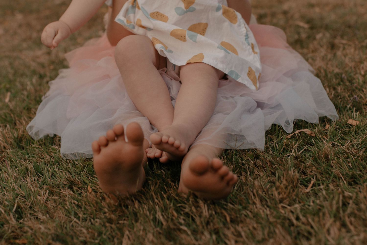 Bare feet of someone wearing a flowy white dress walking through brown grass in a meadow.