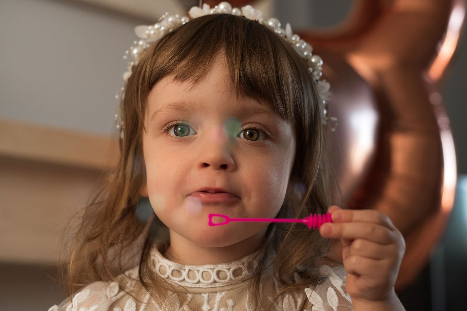 Child wearing white lace headband and dress during special occasion. Blowing bubbles.