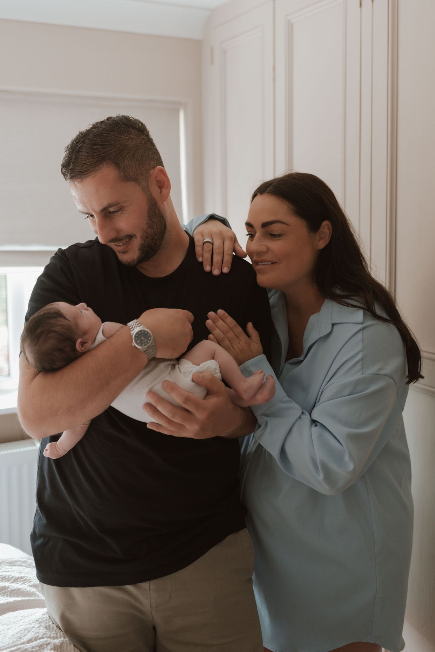 A loving couple admiring their newborn baby together in a bright bedroom with white closets.