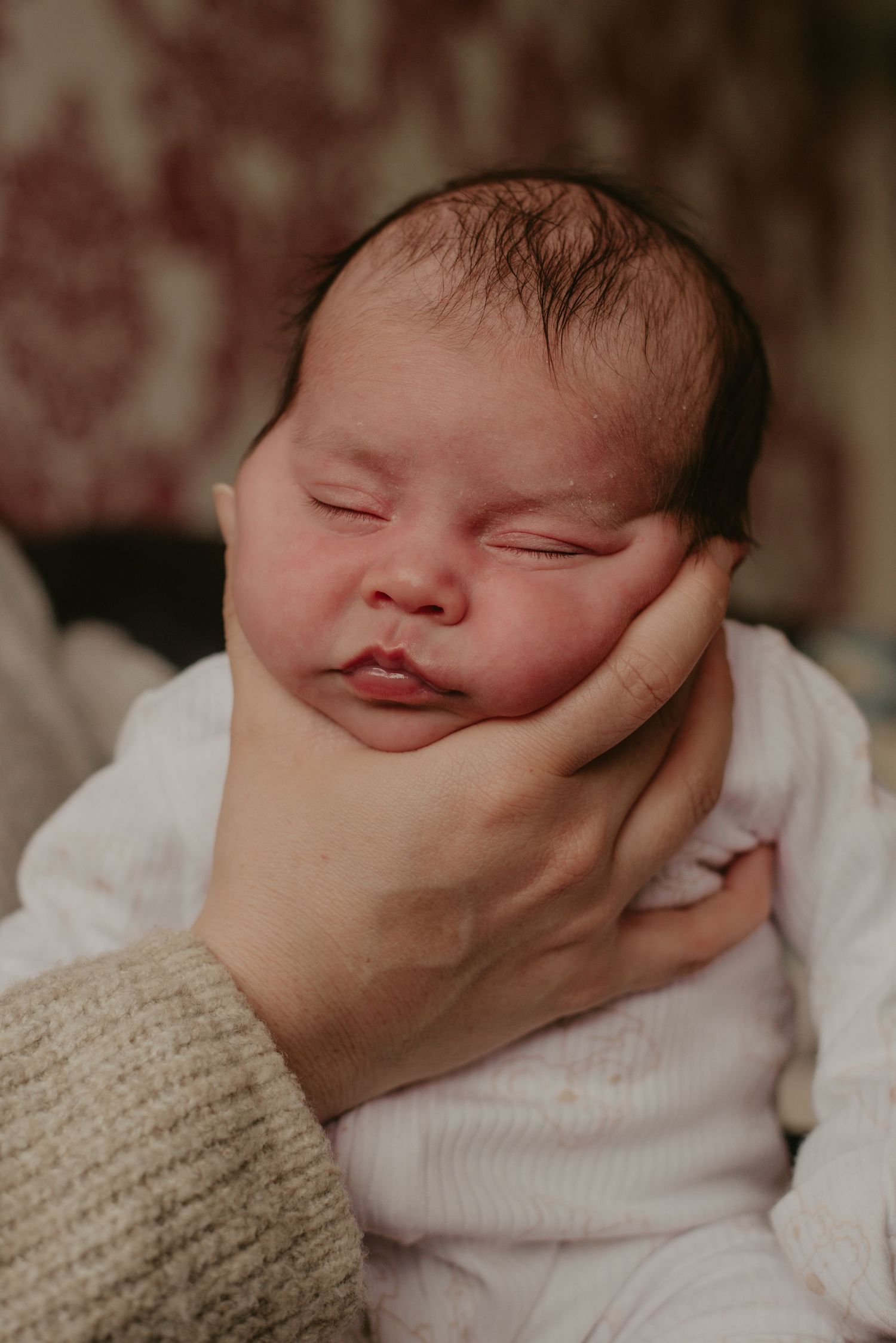 Close-up of a peaceful sleeping newborn baby snuggled in white fabric while being gently cradled.