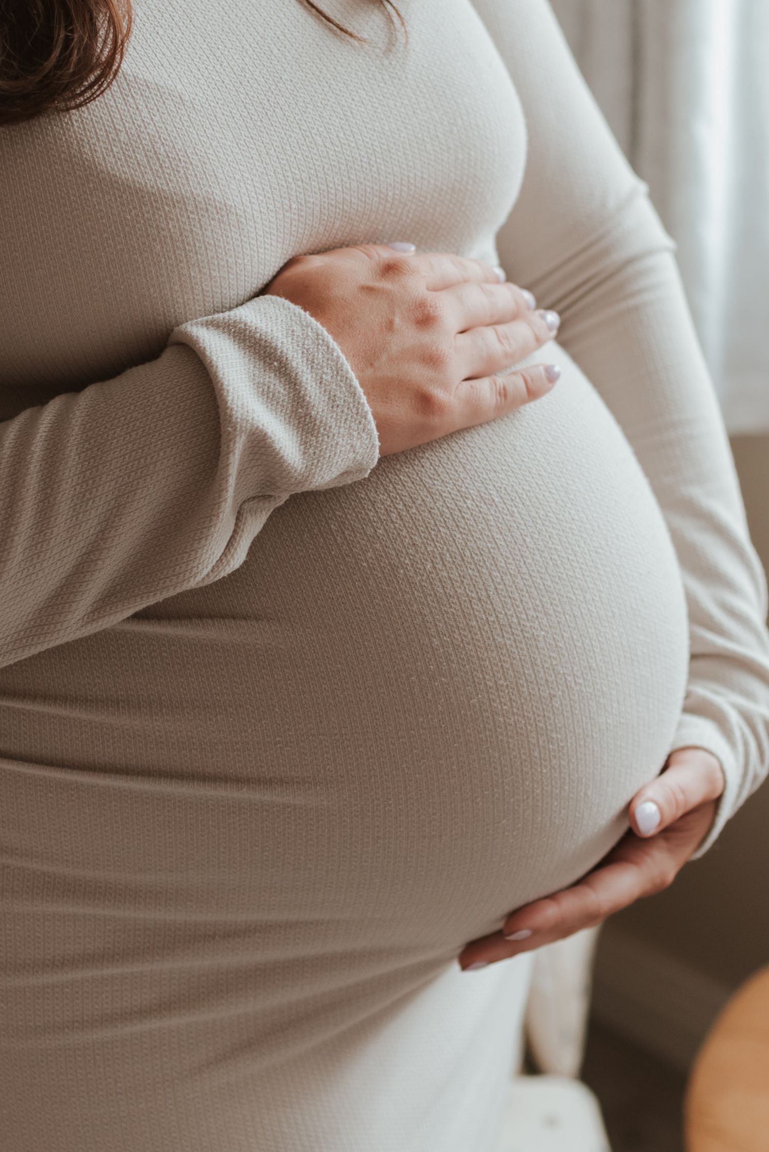 A side view progression of a growing pregnant belly shown in multiple photos wearing a white sweater.