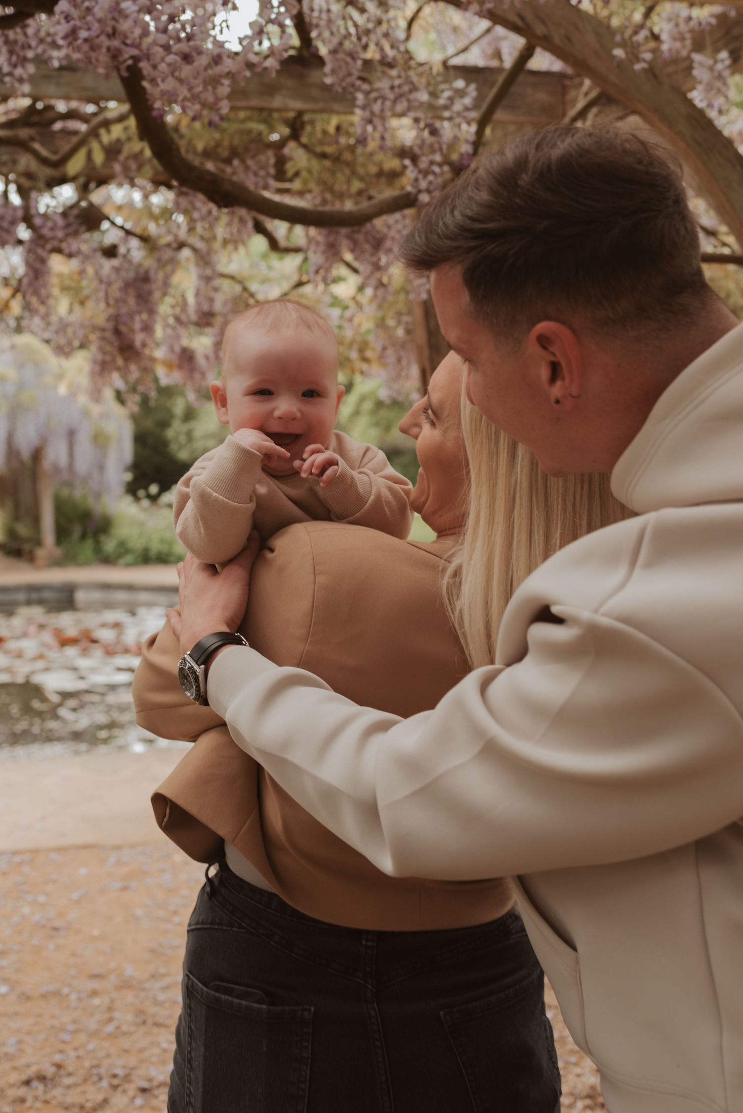 A couple holds a smiling baby under blooming cherry blossoms during springtime.
