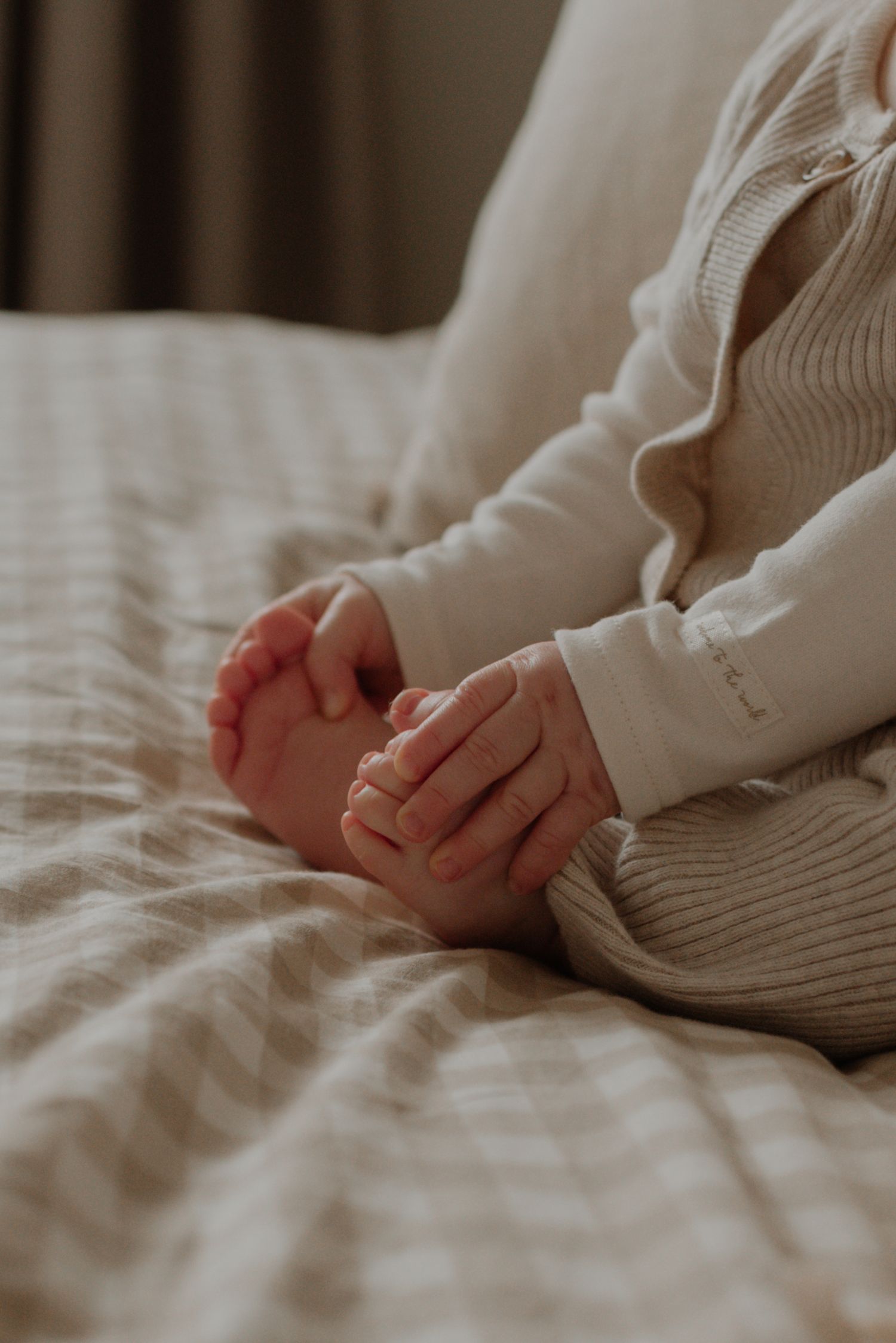 Close up view of tiny newborn baby feet wrapped in soft white blanket on neutral bedding.