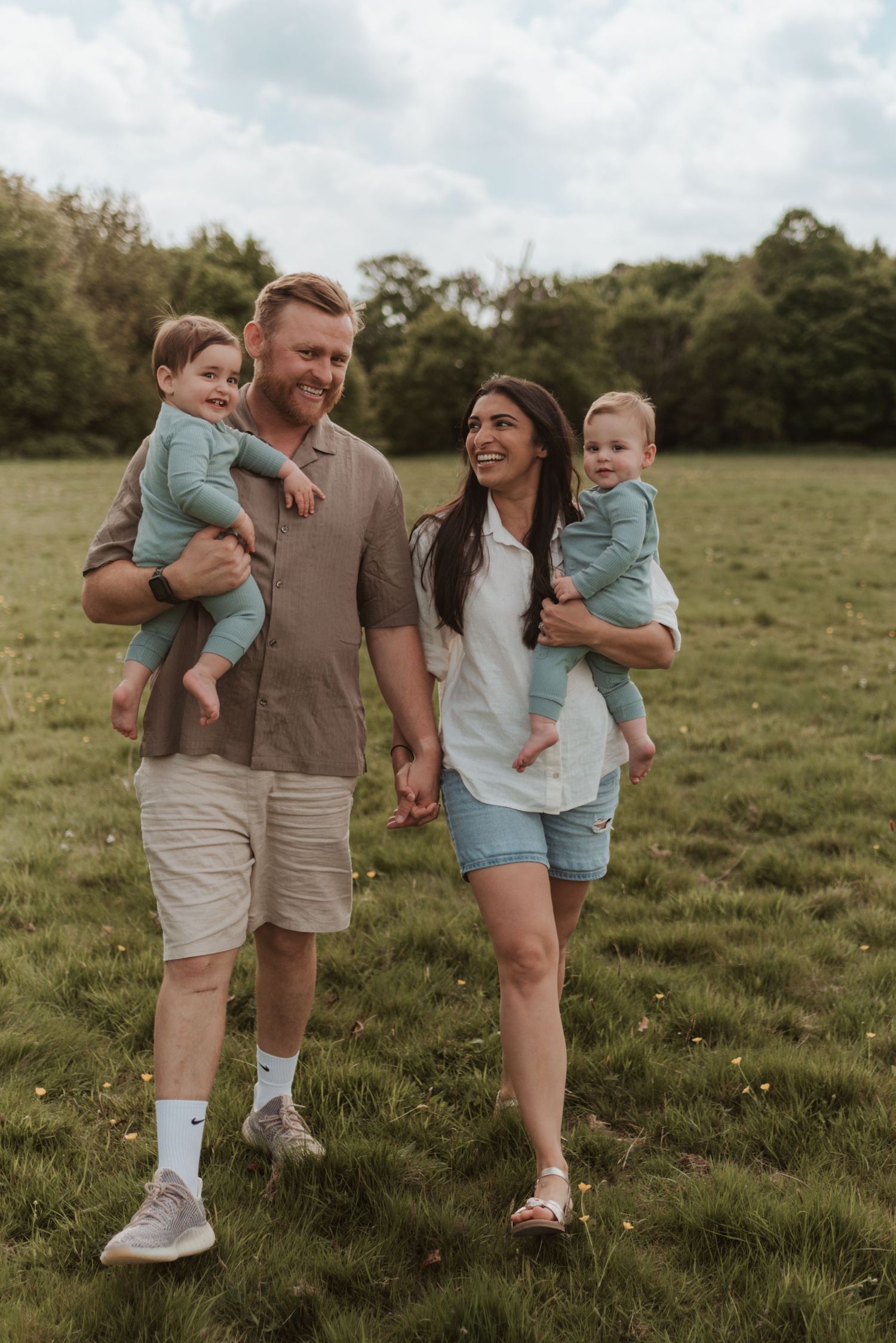 A happy family enjoys a walk together across a green field on an overcast afternoon.