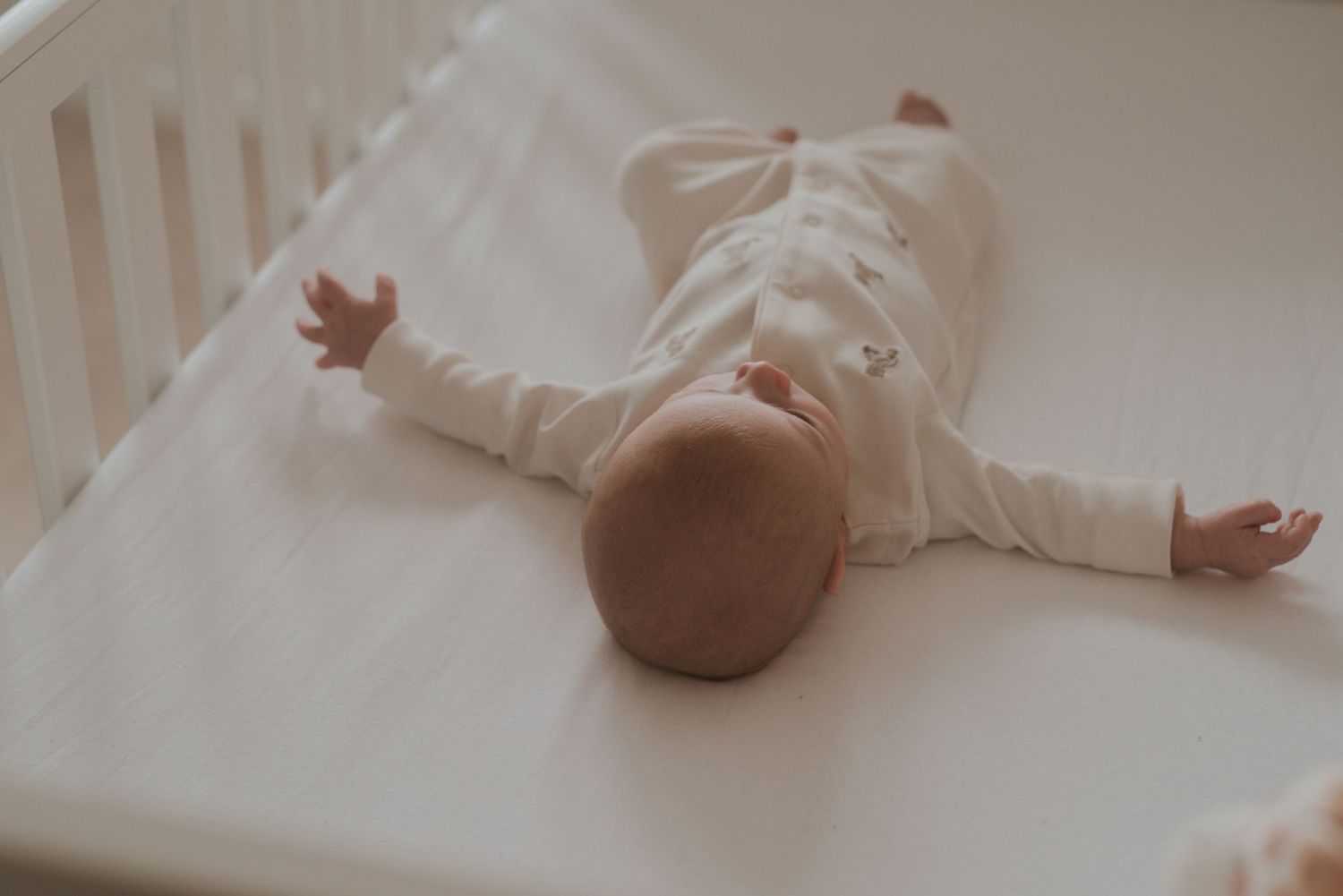 Newborn baby lying peacefully on white bedding with natural window light.
