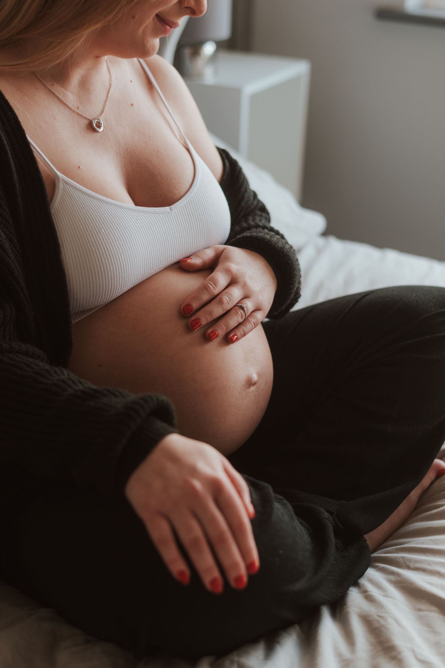 A close-up maternity photo showing hands cradling a pregnant belly while sitting on white bedding.
