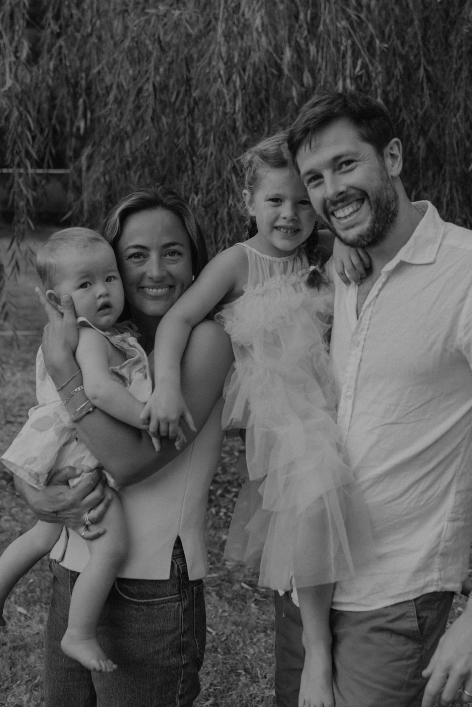 A joyful family photo session outdoors showing candid moments of affection and laughter in black and white.