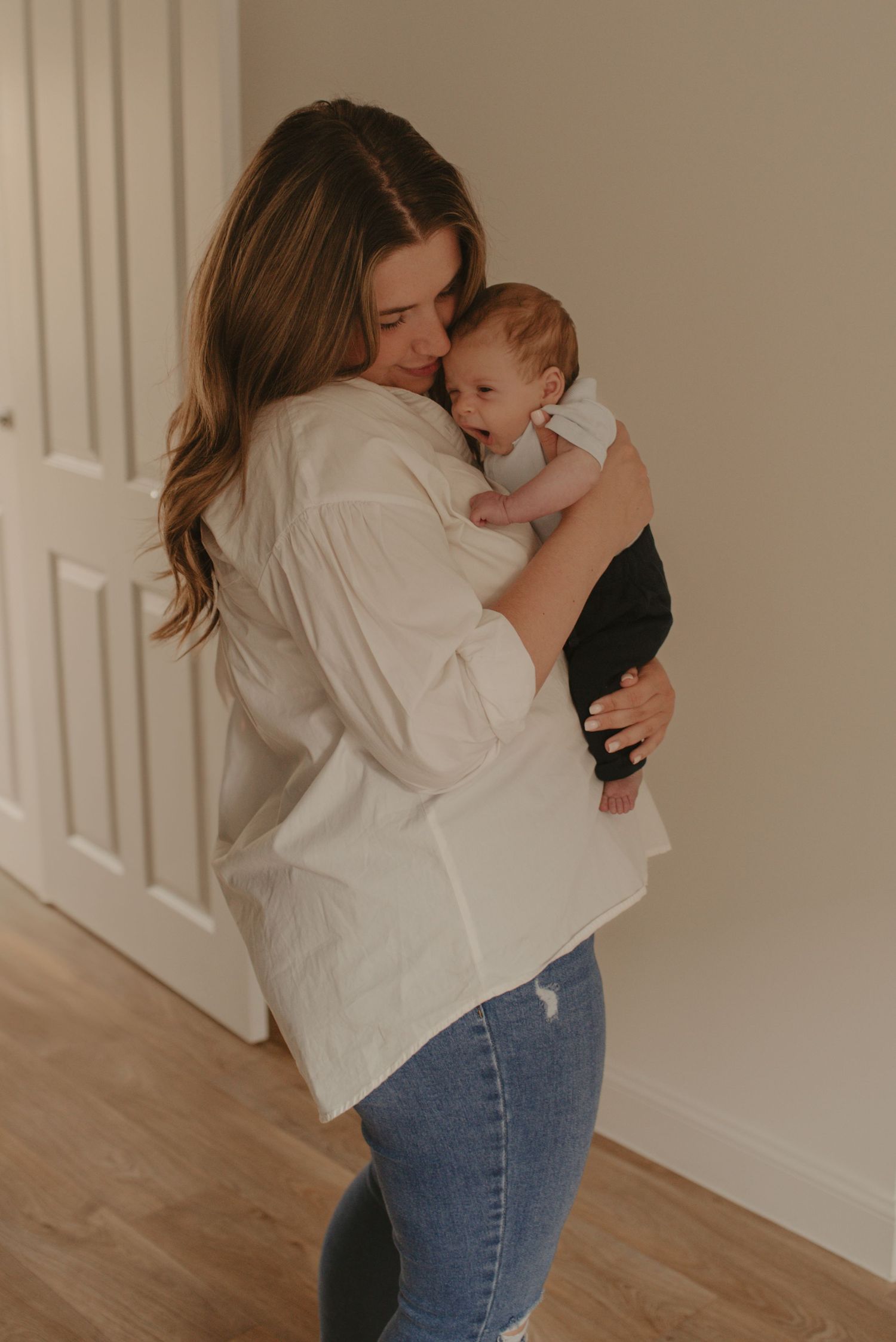 Tender moment between parent and newborn in a bright, minimalist interior with wooden floors.