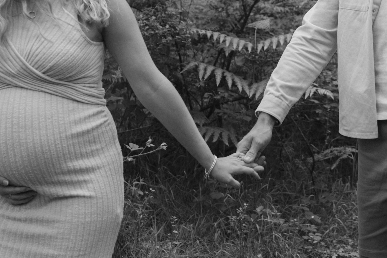 A black and white photo of joined hands with a baby bump visible against decorative bunting.